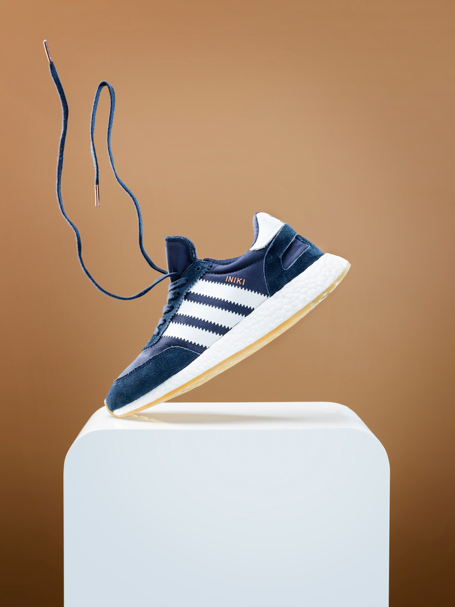 Einzelner Schuh steht nur mit der Spitze auf weißem Tische vor farbigem Hintergrund, Schnürsenkel schweben in der Luft