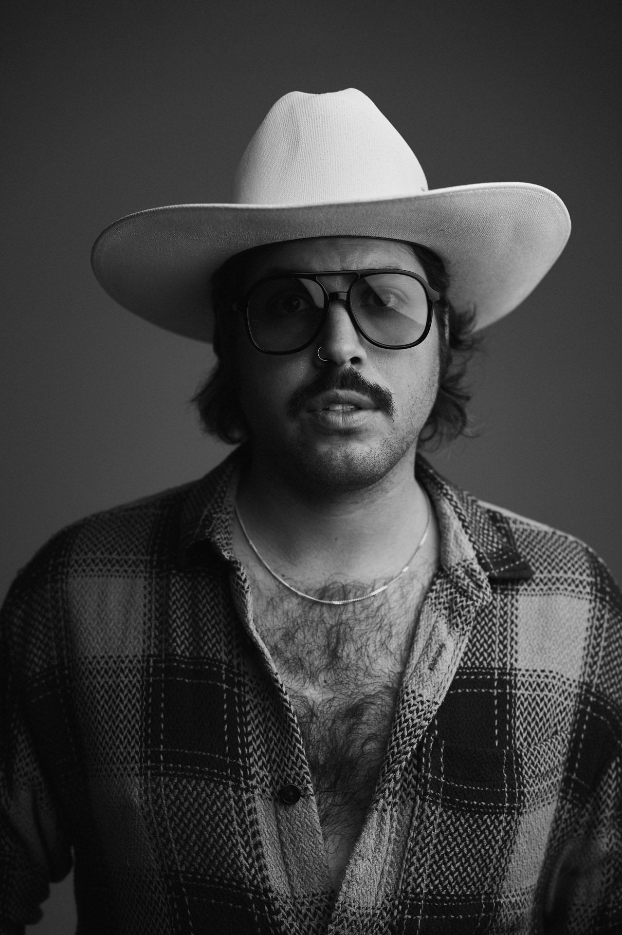 Schwarz-Weiß-Porträt eines Mannes im Studio mit Cowboyhut, Brille und Hemd. Fotografiert von Michael Kreyer – ausdrucksstarke Studiofotografie mit klarer, grafischer Lichtführung.