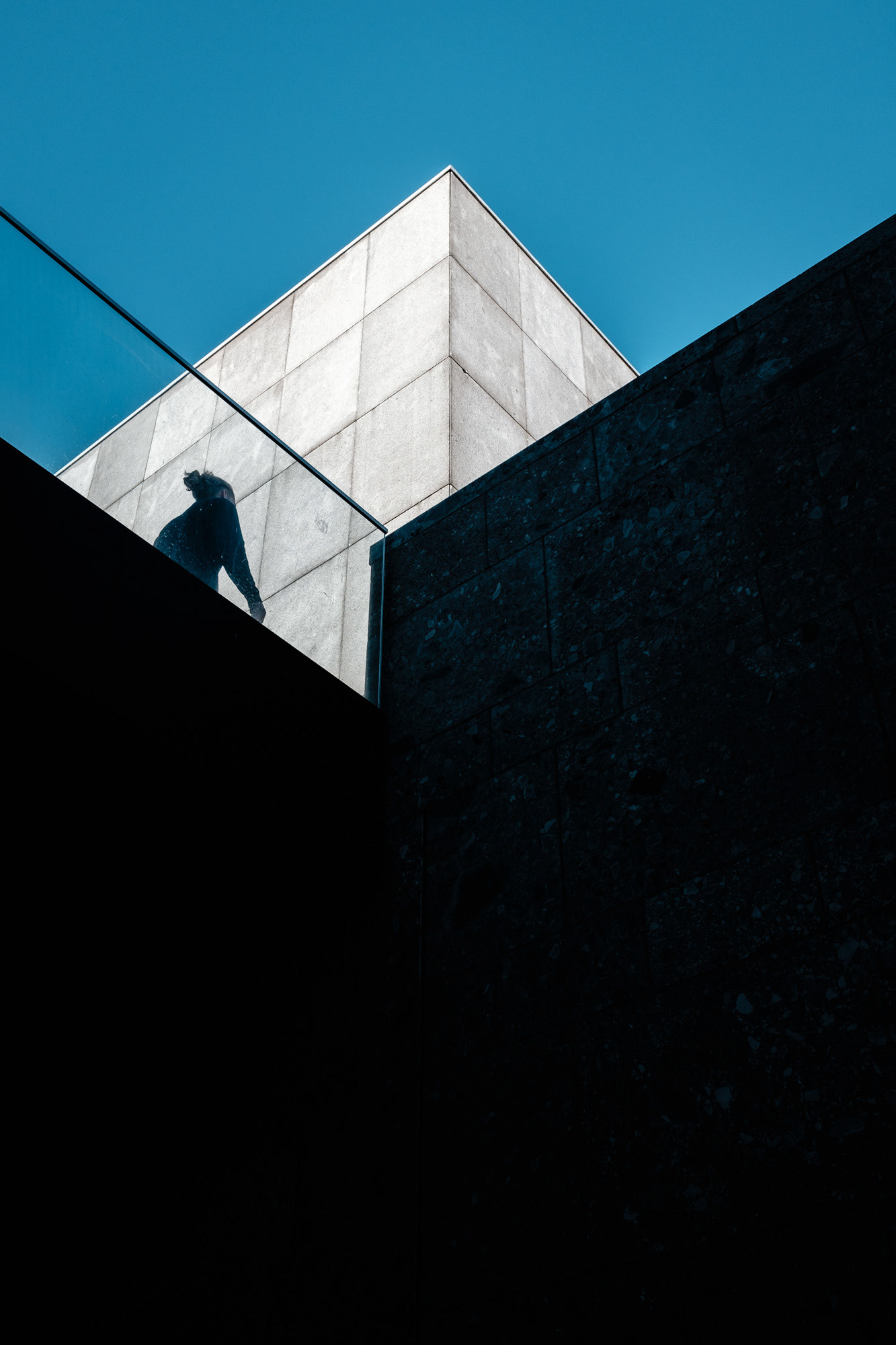 Geometrische Gebäudeformen vor blauem Himmel mit Person