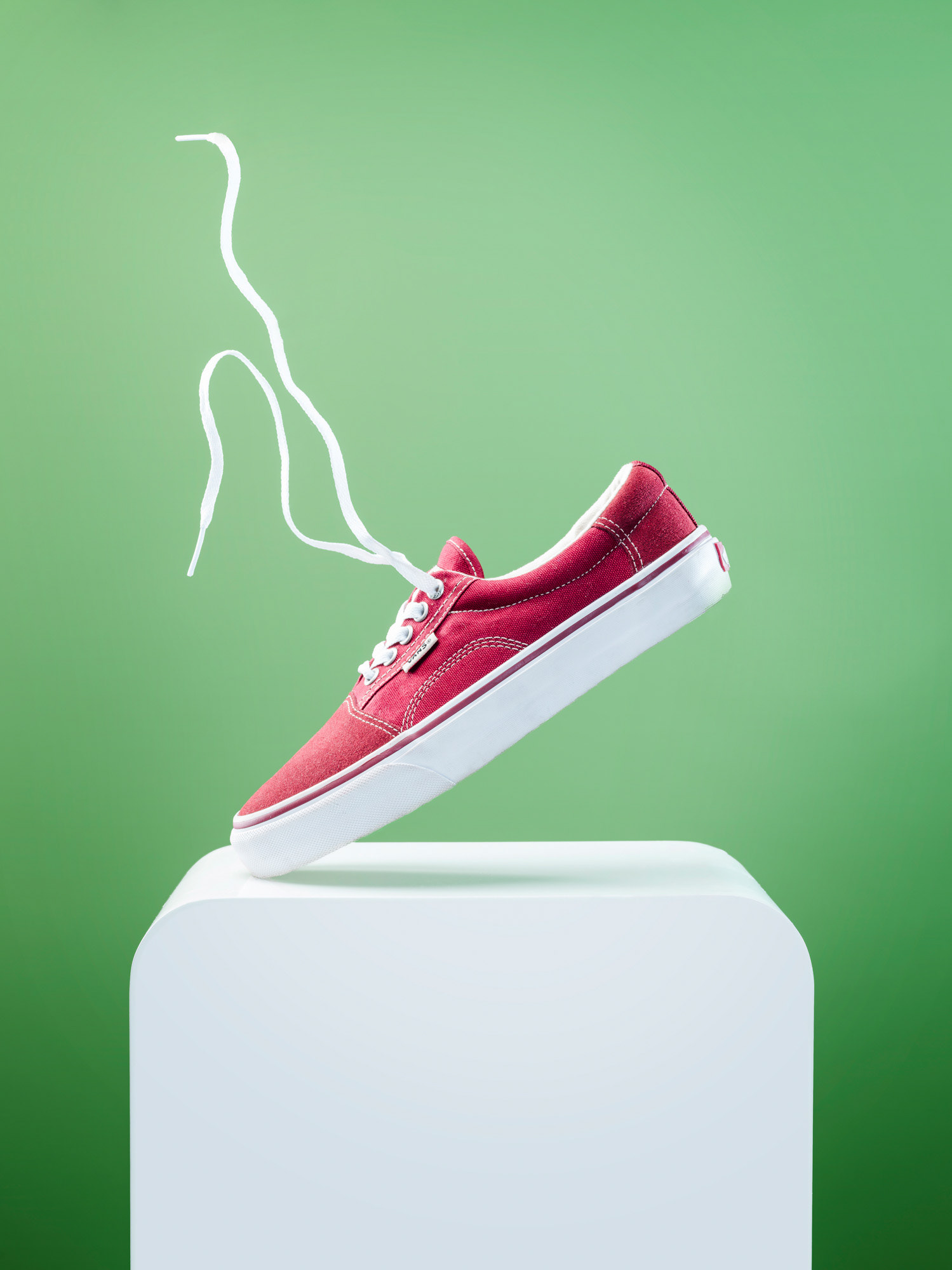 Einzelner Schuh steht nur mit der Spitze auf weißem Tische vor farbigem Hintergrund, Schnürsenkel schweben in der Luft