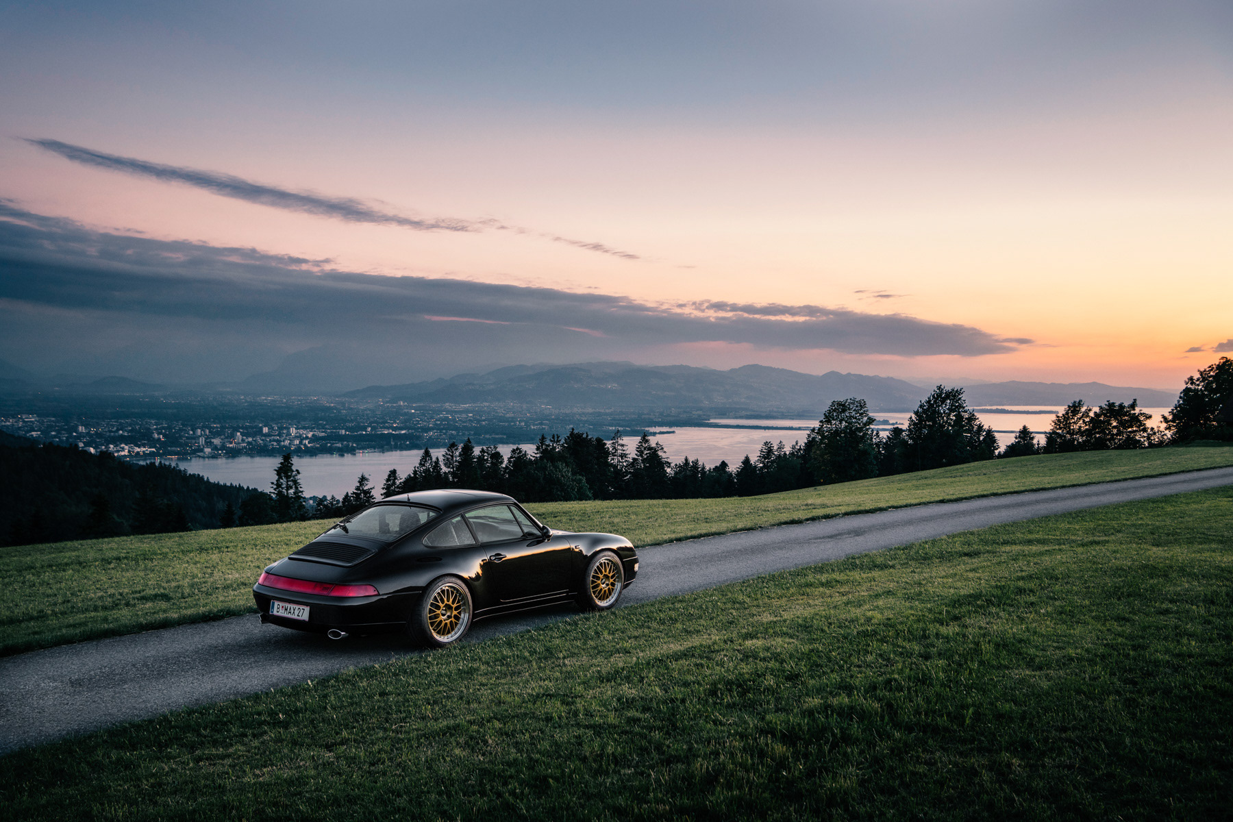 Auto Porsche vor Skyline mit See bei Sonnenuntergang auf Straße