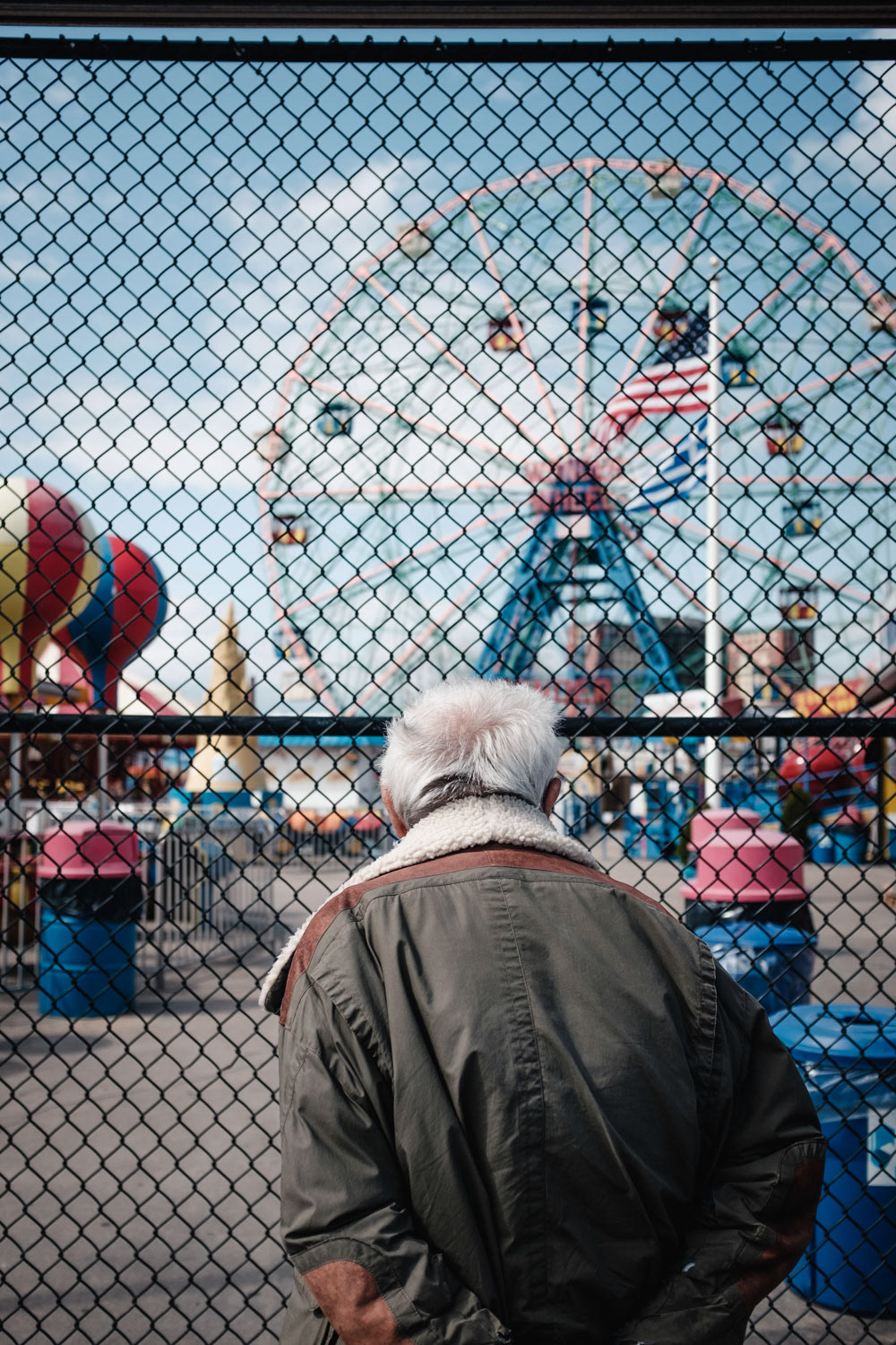 Mann vor Zaun schaut auf Riesenrad und USA Flagge