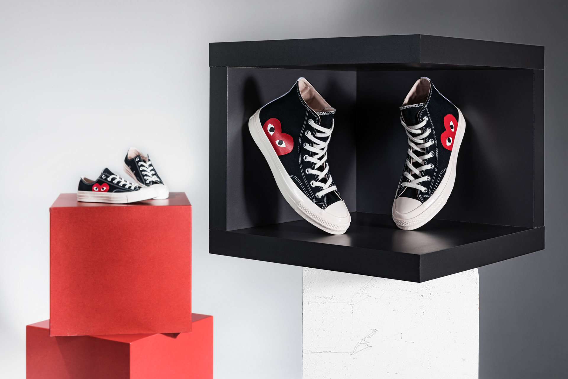 Ein paar Schuhe im Hintergrund auf roten Blöcken ein paar Schuhe im Vordergrund in Kasten vor weißem Hintergrund