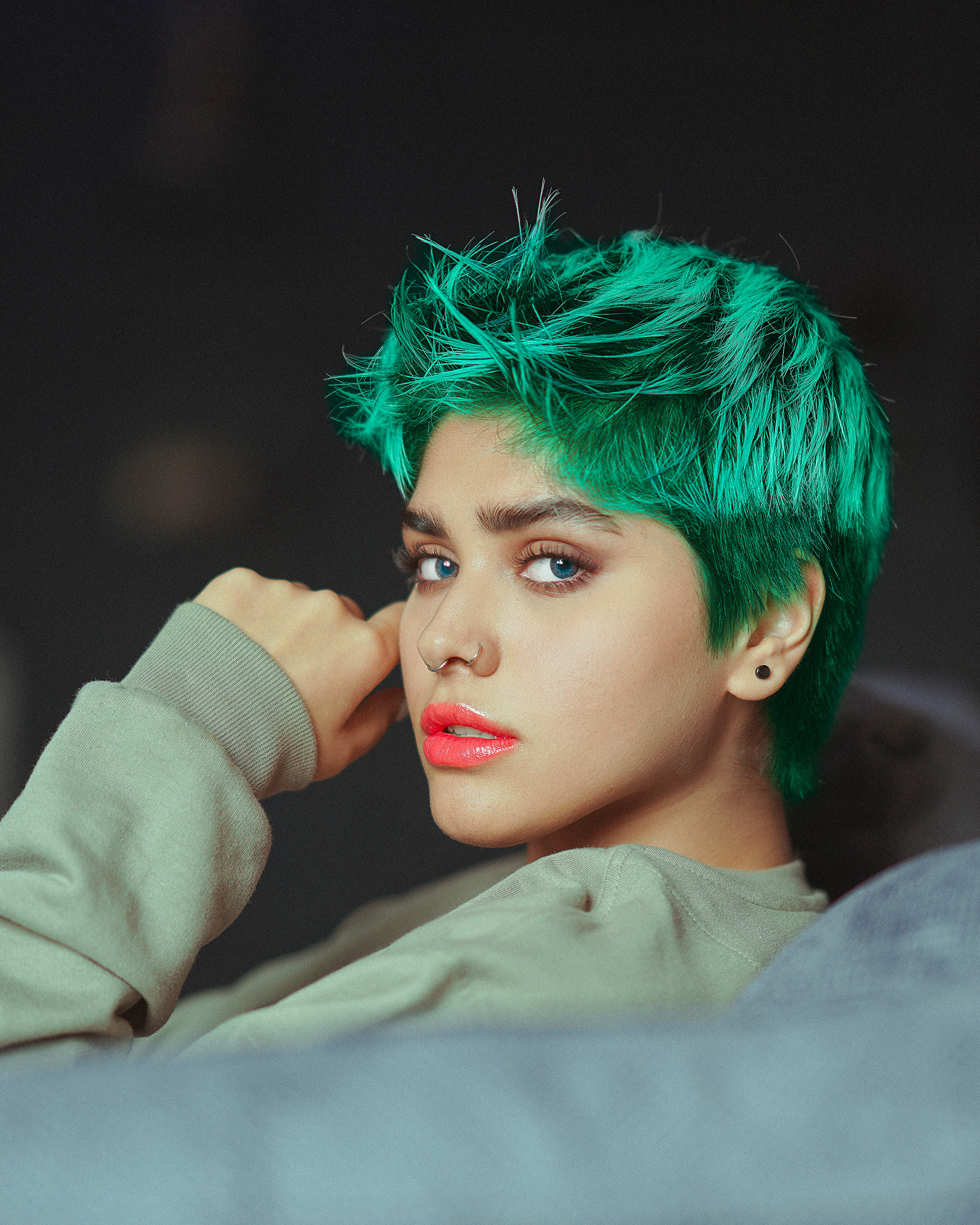 Close-up portrait of young person with bright green hair, blue eyes, nose ring, and coral lipstick.