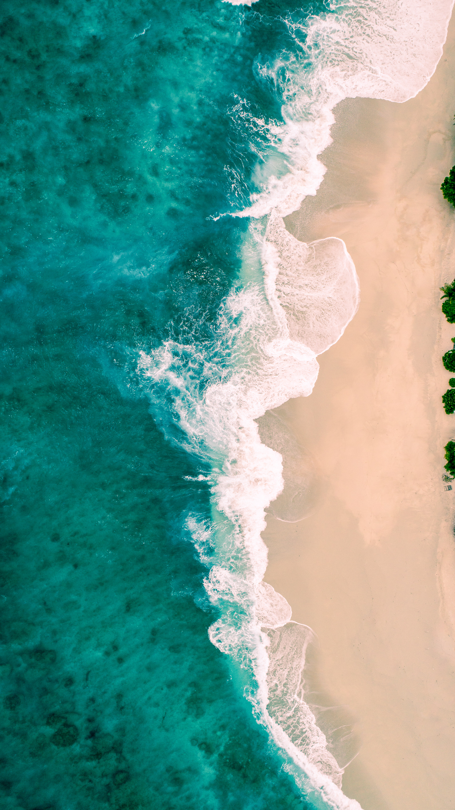 Aerial view of turquoise ocean waves crashing onto sandy beach.