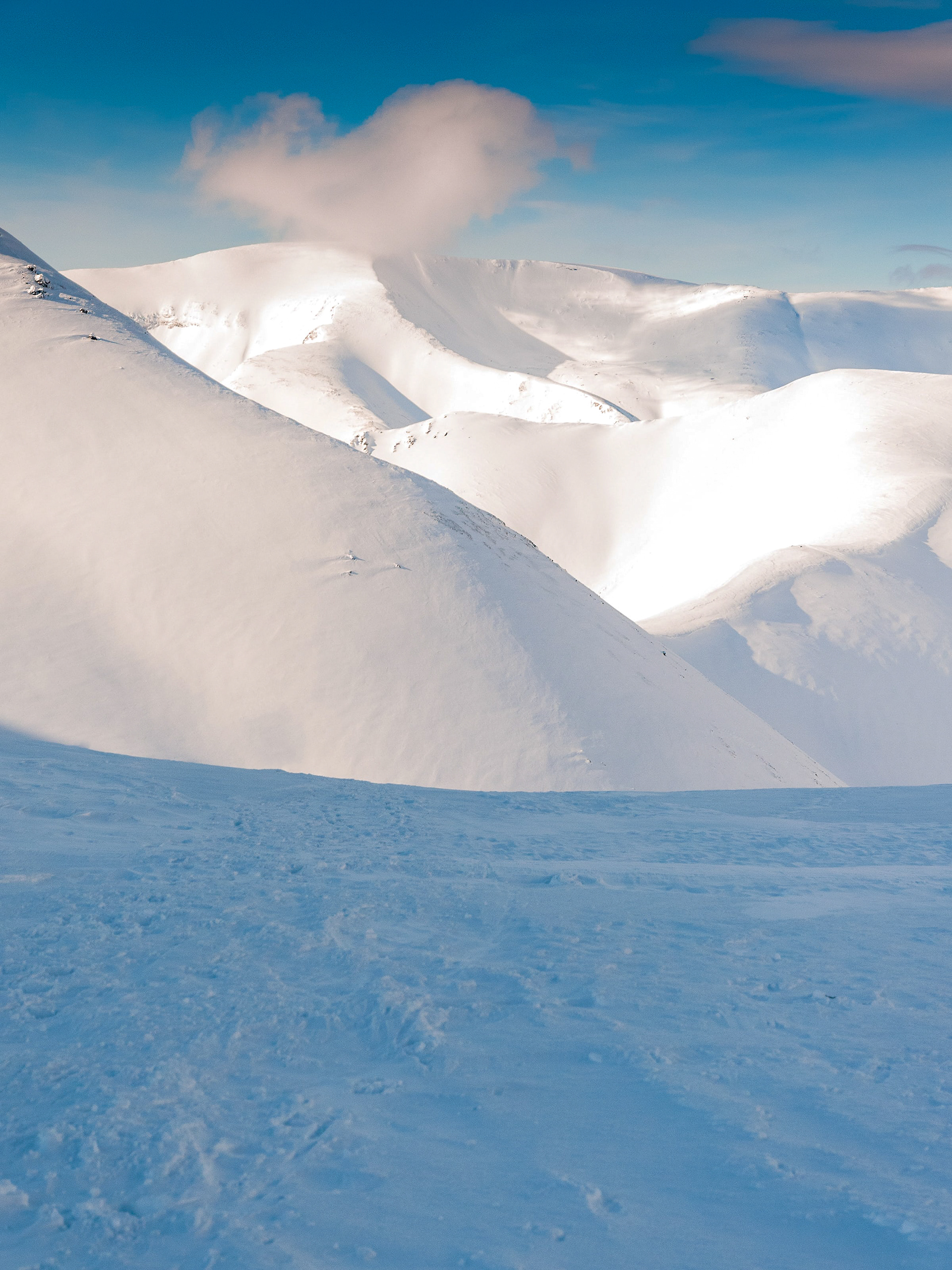Snow-covered mountain range under clear blue sky with single fluffy cloud above peaks.