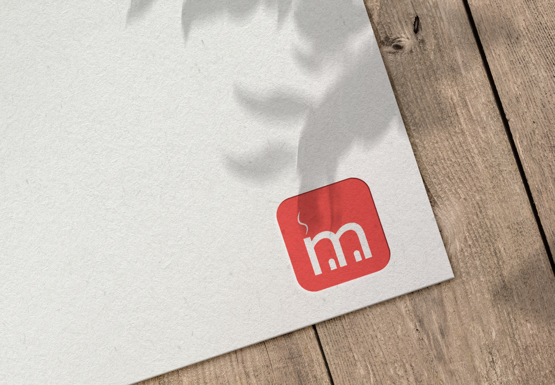 Red square logo with rounded edges on paper, featuring white lowercase m and wavy steam-like line above.