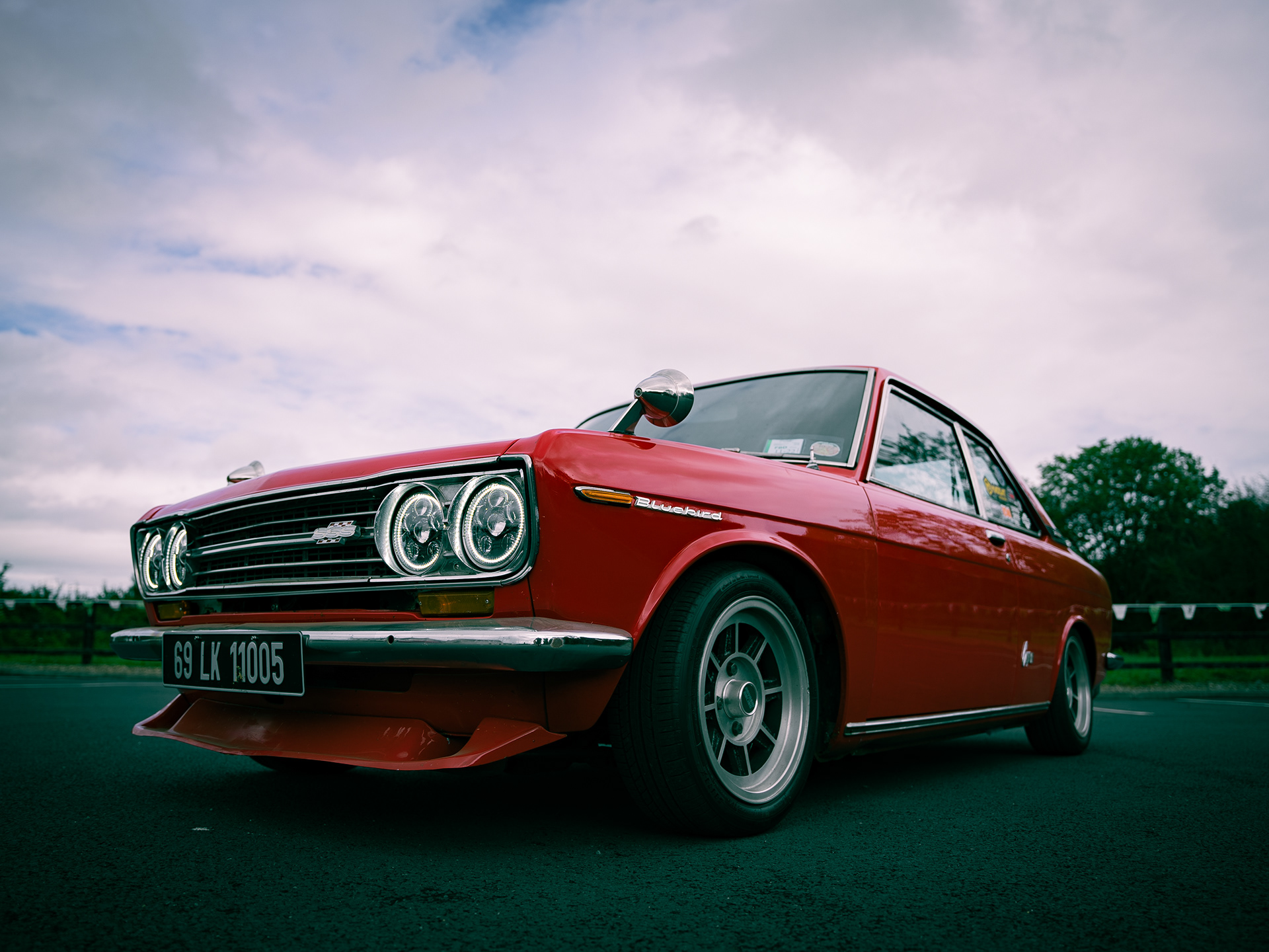 Low-angle photo of red vintage Nissan Bluebird car highlighting front grille and headlights.