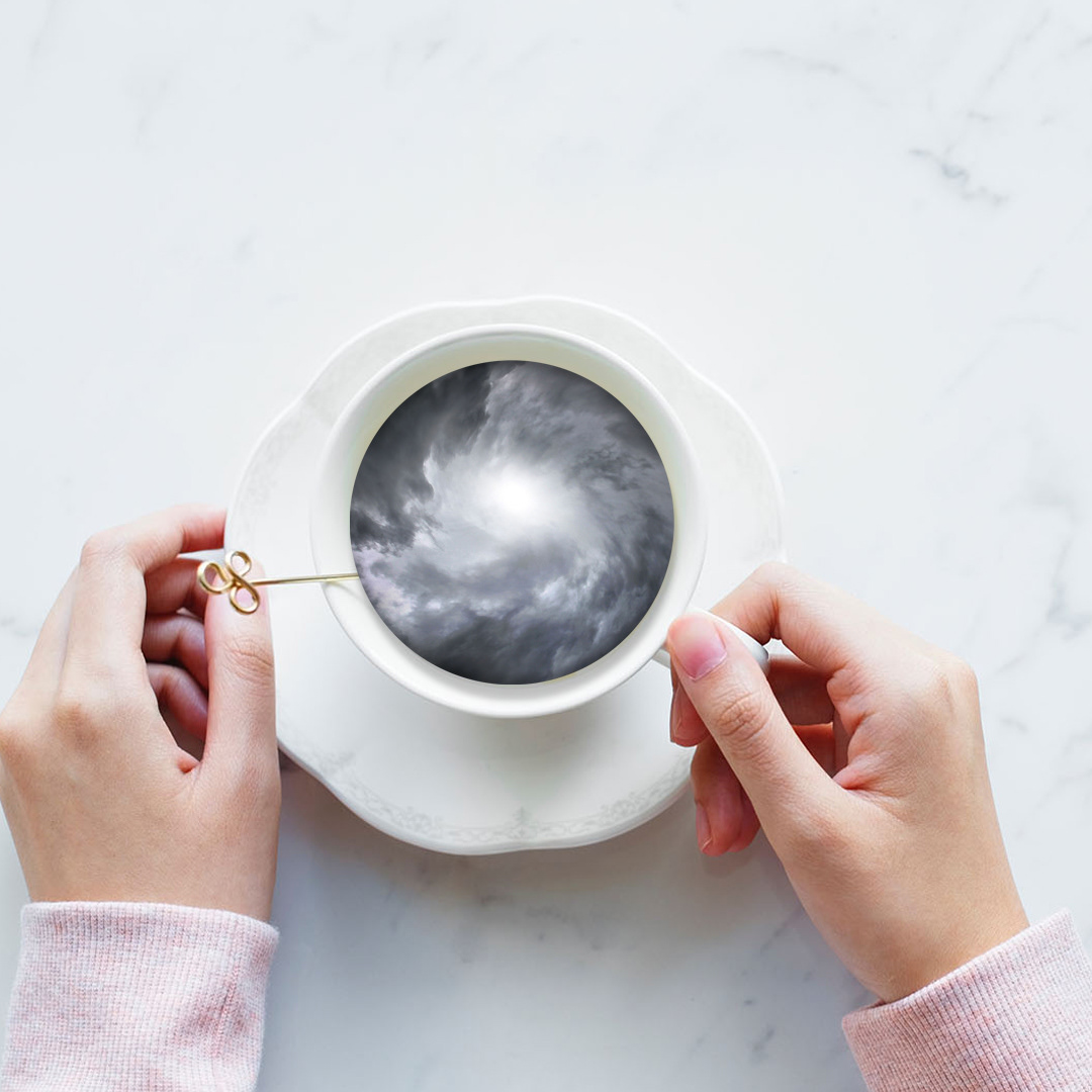 Hands holding teacup with swirling stormy sky inside.