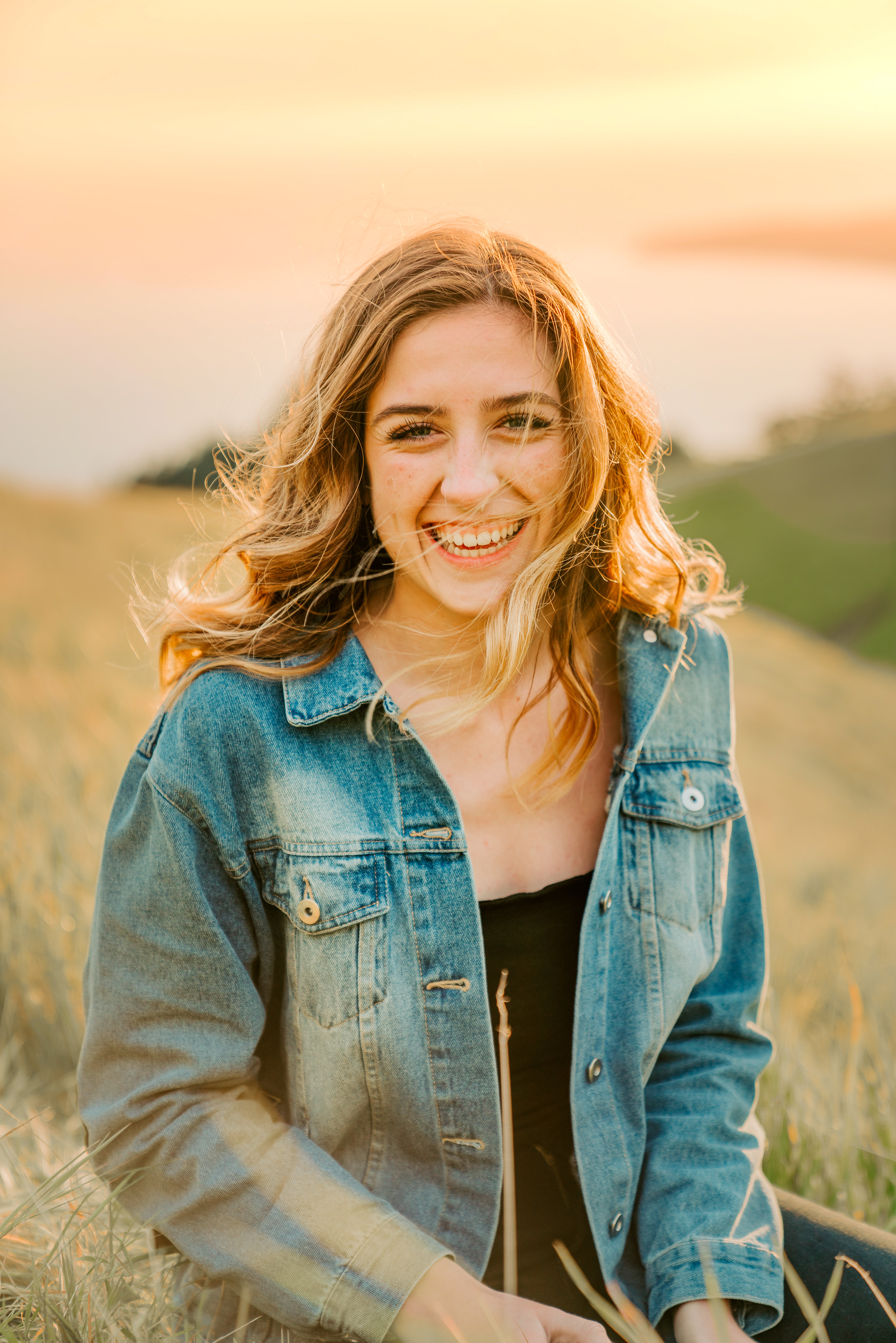 Smiling woman in denim jacket outdoors at sunset.