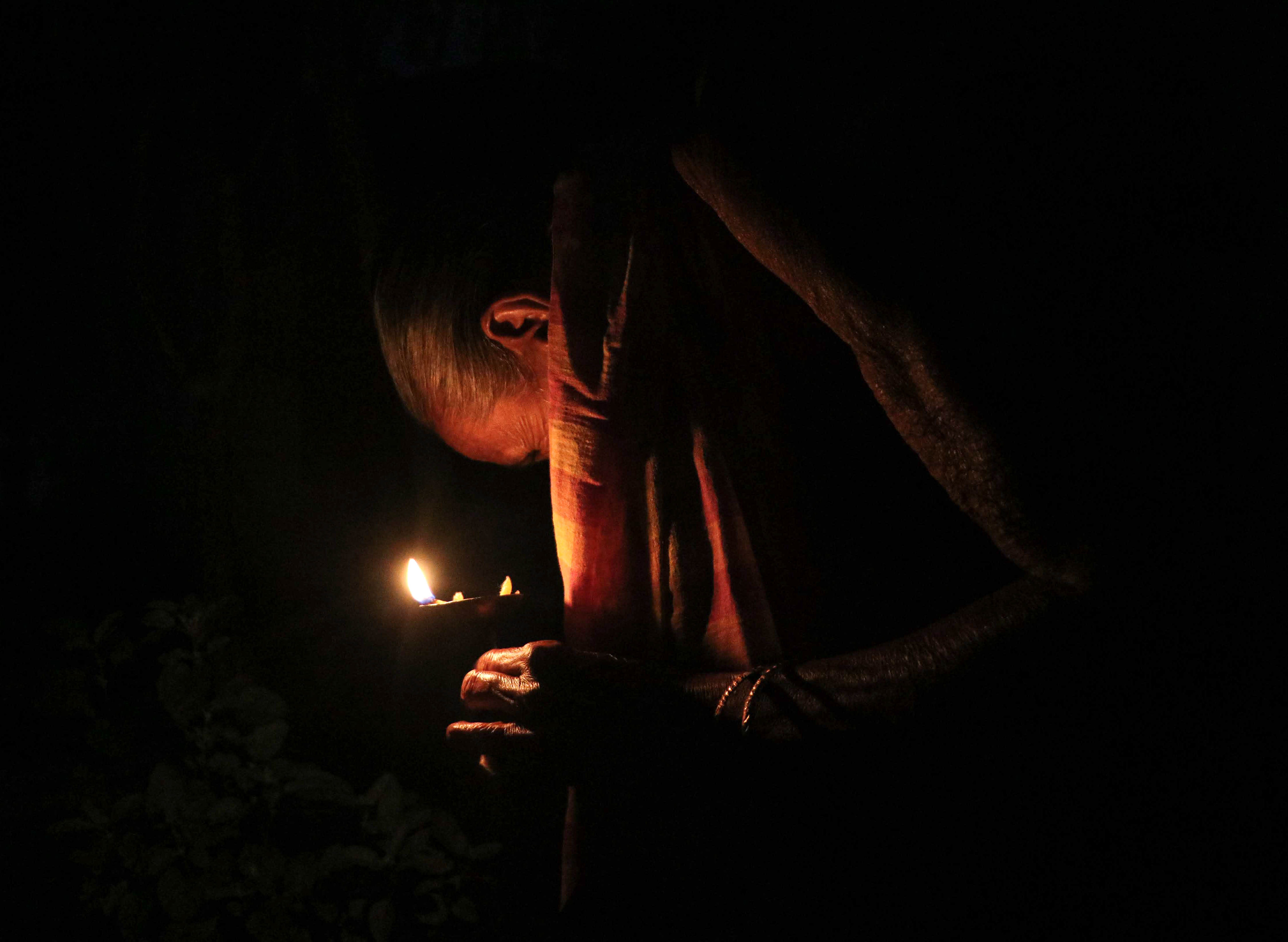 An elderly woman offers evening prayer with an oil lamp