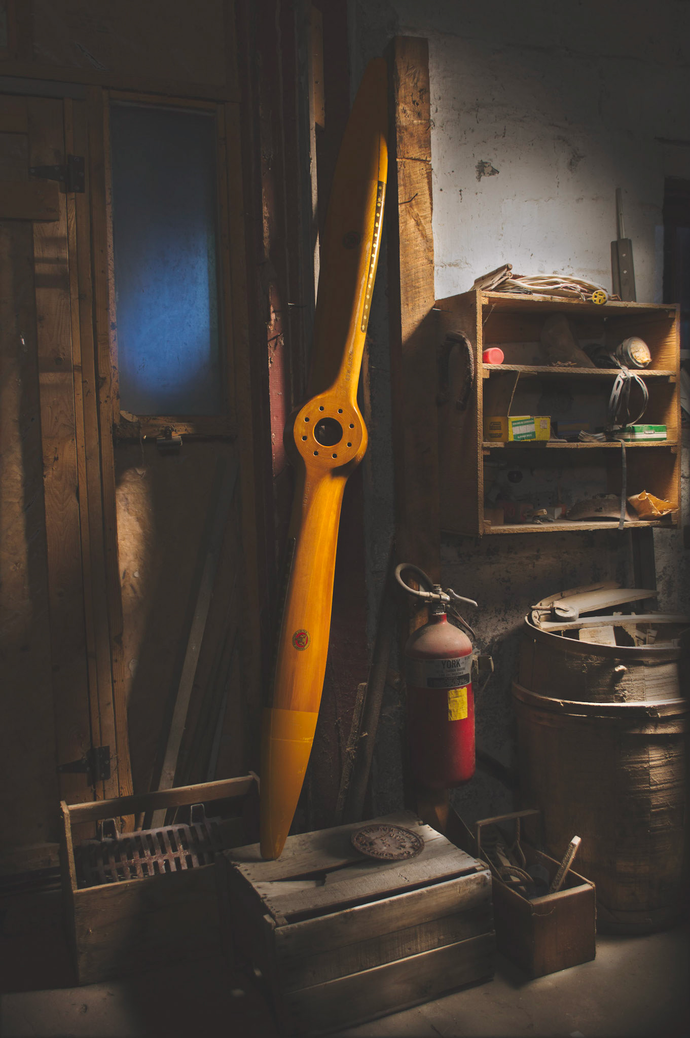Wooden propeller from a Gypsy Moth leaning against a hangar wall.