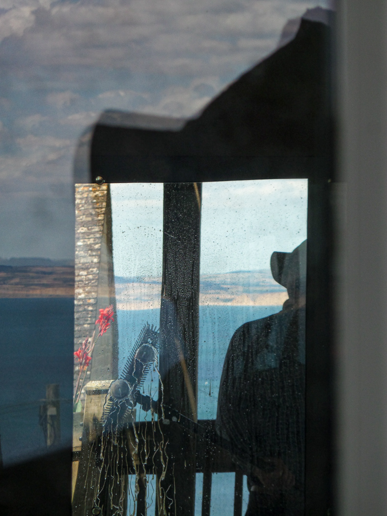 A windows cleaner is shown cleaning a window with a coastal landscape reflected in the glass