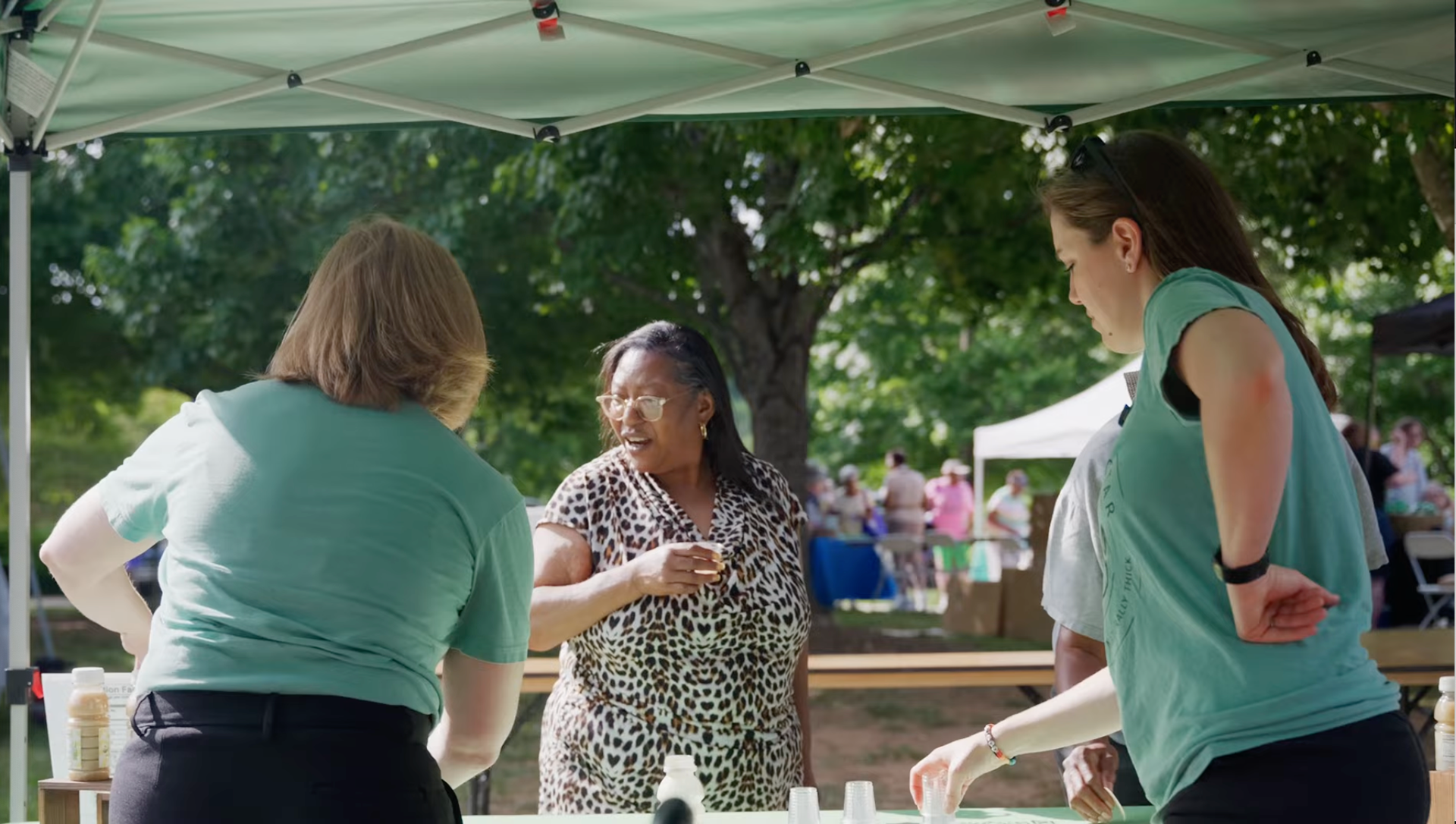 Ally Roberts of Naturally Nectar pouring a sample for a visitor at her table during the Triad Elder Abuse Awareness Walk at Triad Park.
