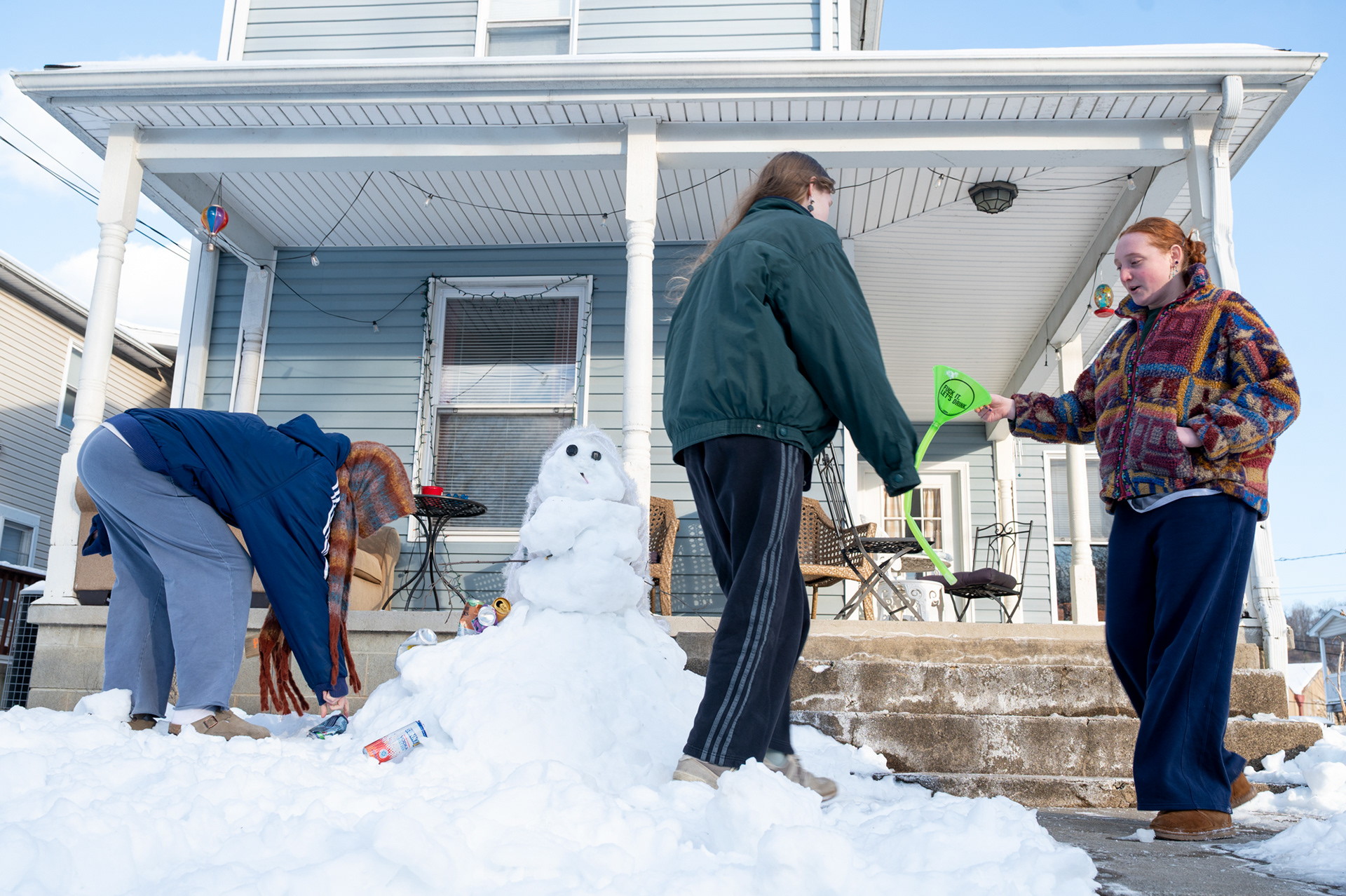 Jill Woodruff (left), Sadie McClinchie (center), and Olivia Demaree (right) add decorations to their snowman in front of their college home in Athens, Ohio, on Wednesday, Jan. 28, 2026. After learning that classes were canceled earlier in the week, the roommates spent time outside playing pong, drinking socially, and building a snowman rather than focusing on schoolwork. With no in-person classes to attend, the group returned to the snowman over the next few days, shifting their attention toward nearby social activities and creative memories during the storm.