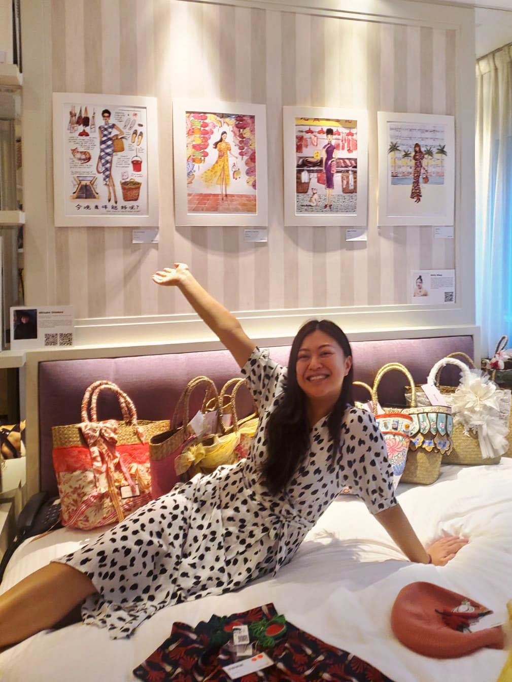 Hong Kong woman artist Kitty Wong sitting in Lanson place hotel bed with cream striped wallpaper with paintings behind her during exhibition at Art Next