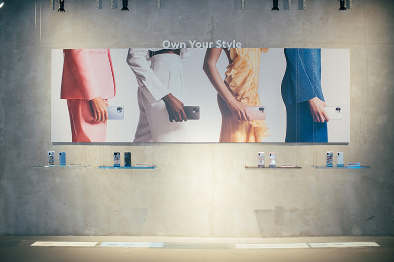 Xiaomi smartphone launch event with large gray photo wall that says "Own Your Style" with smartphone and cases on display