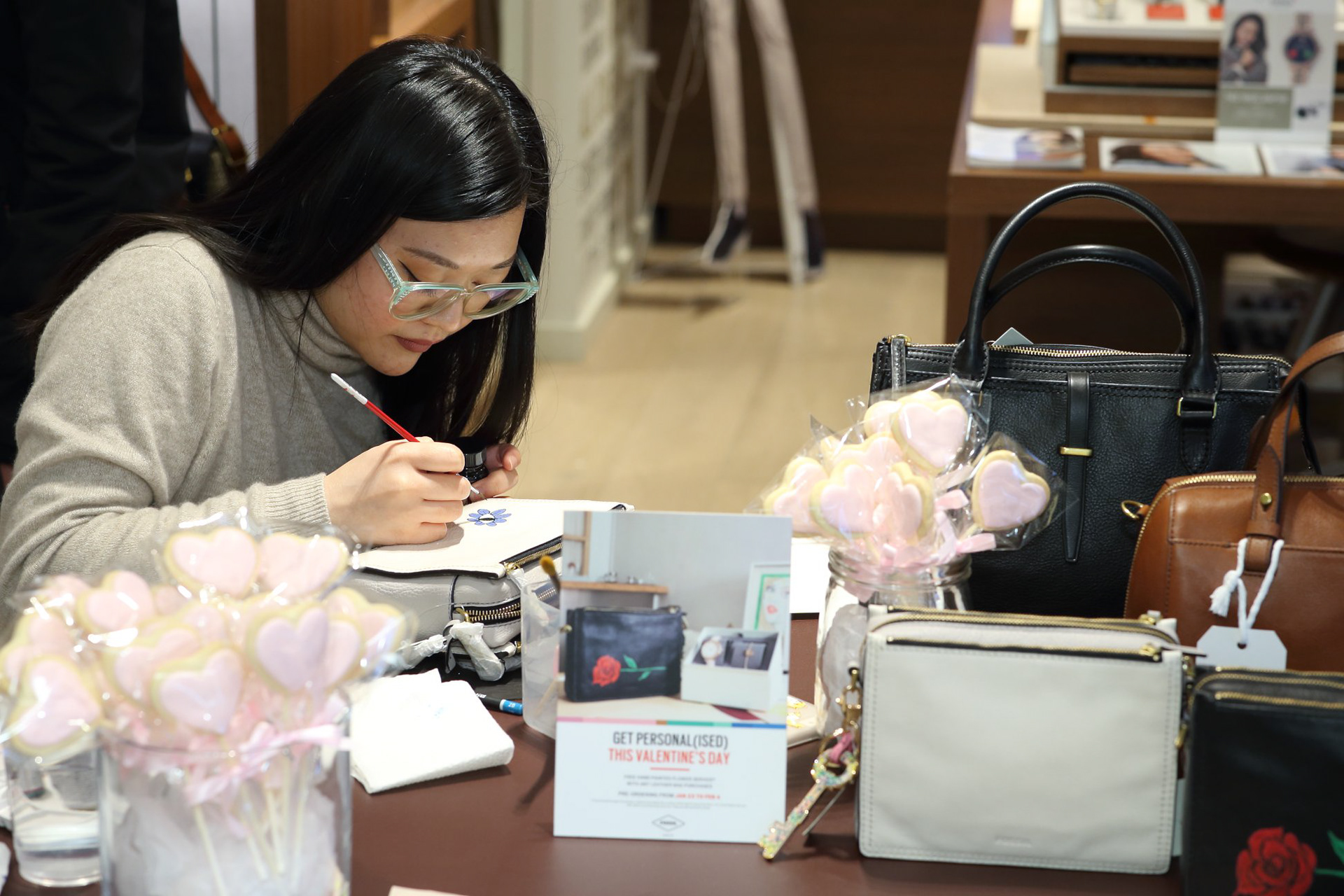 Hong Kong female artist Kitty Wong bending down to paint on a leather bag at a table in Fossil store in Harbour City Mall