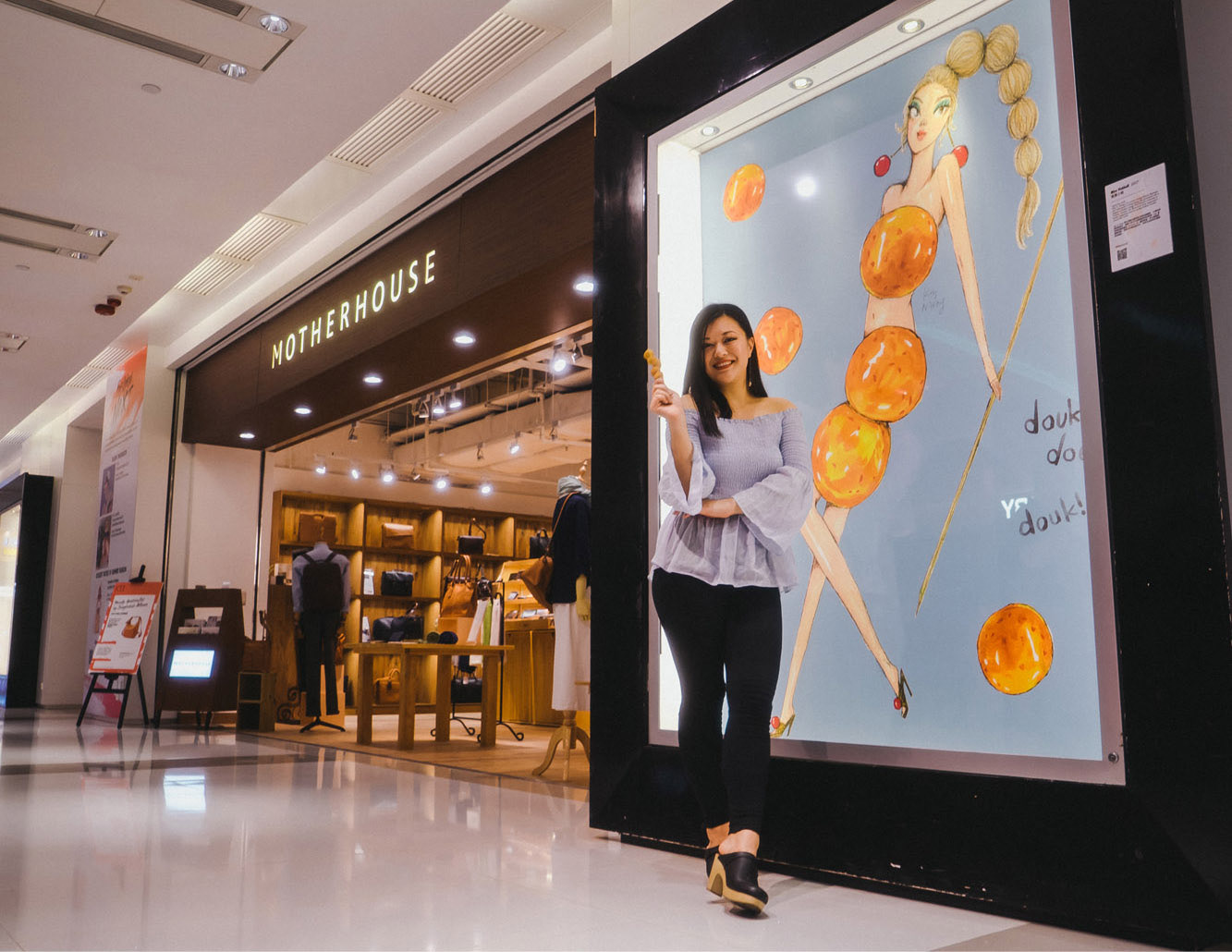 Hong Kong woman artist standing in front of her "Miss FishBall" artwork in a large frame inside K11 shopping Mall