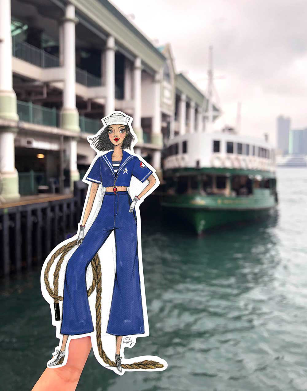 Hand holding sticker of a star ferry sailor woman with background of green ship docked in Hong Kong Central pier