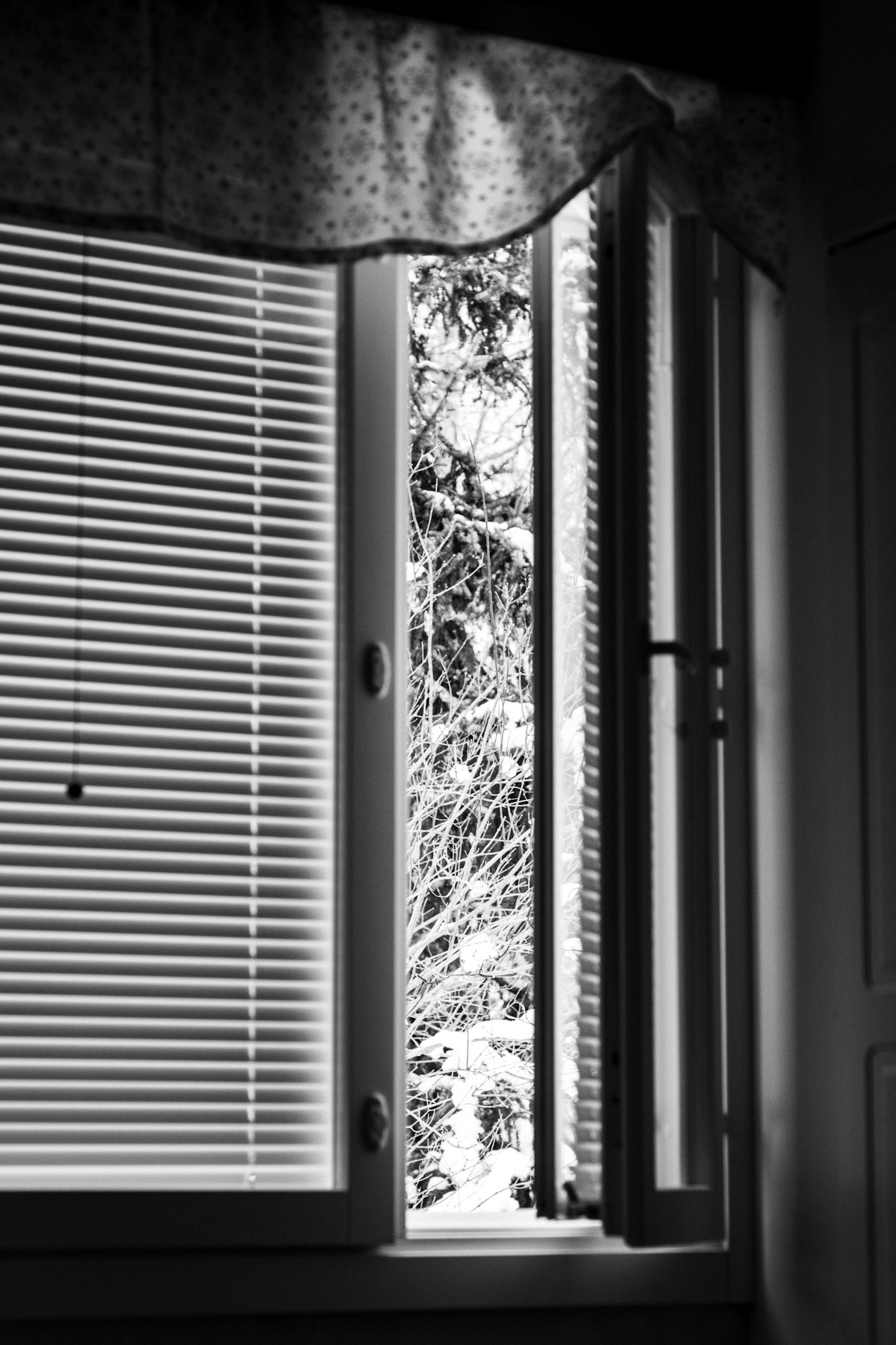 A black-and-white photo of an open side window in an otherwise dark bedroom. 