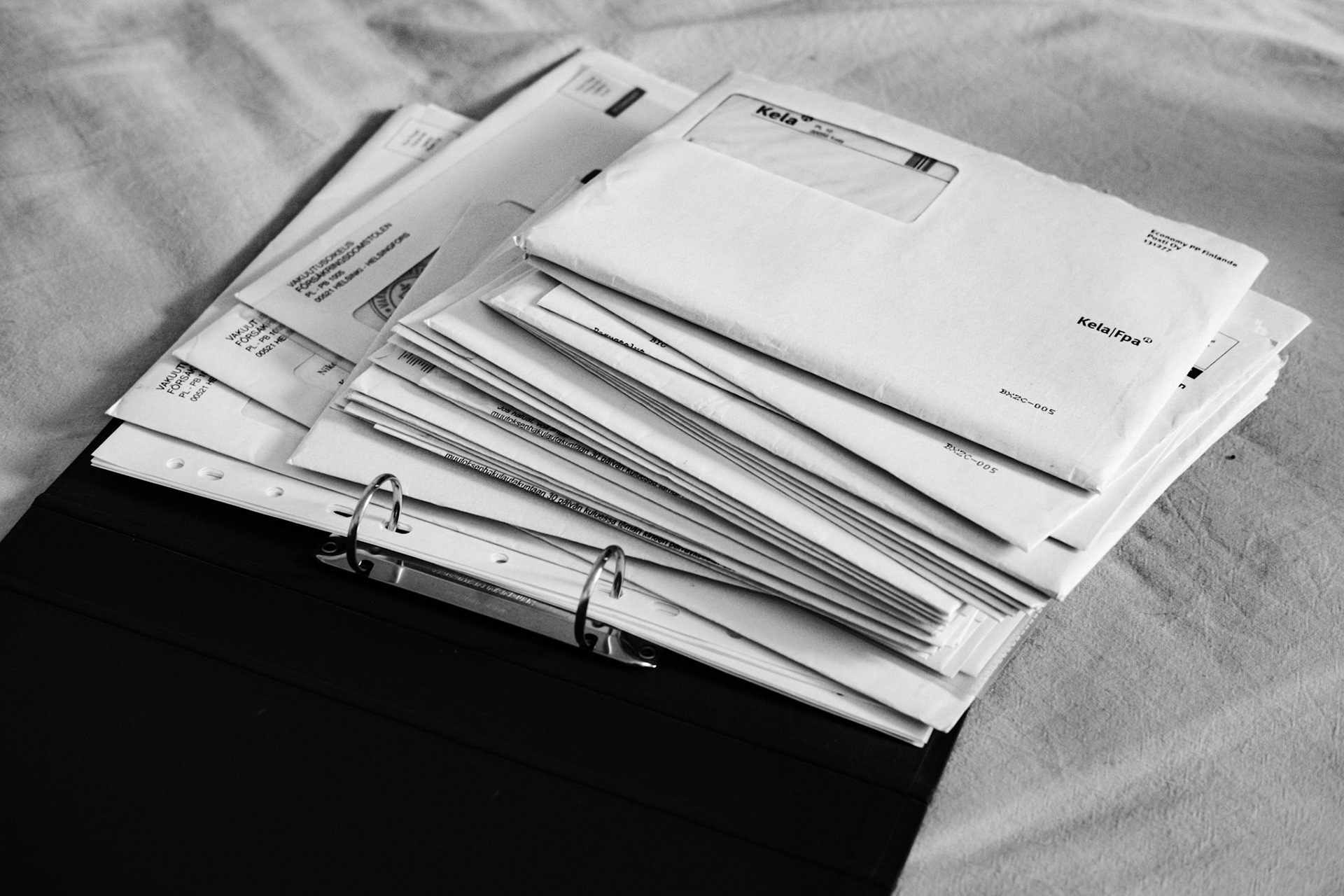 A black-and-white photograph of a pile of papers and envelopes on top of a folder.