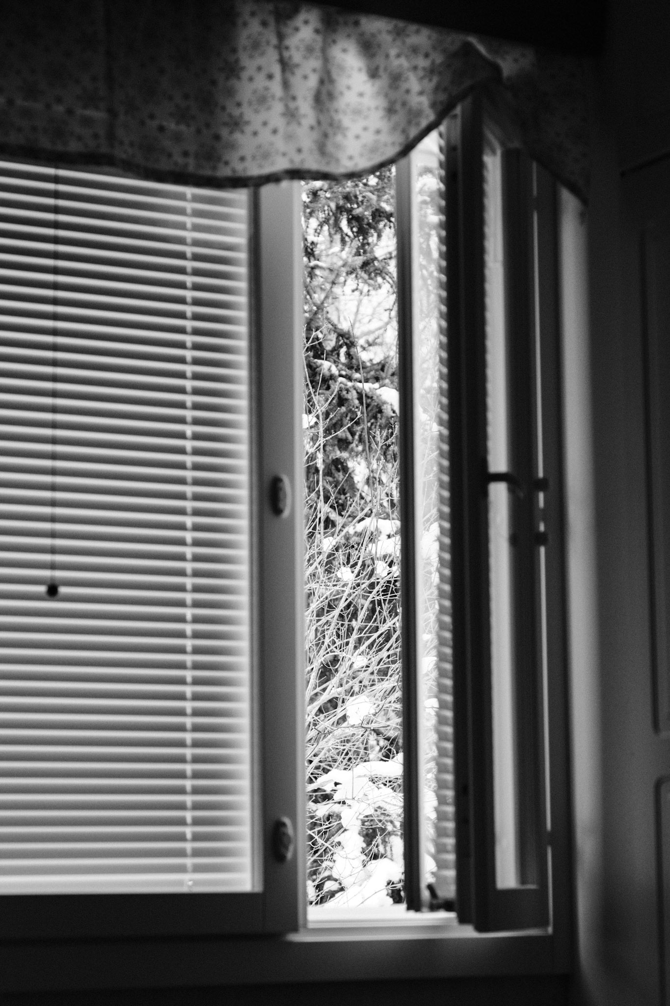 A black and white photo of an open side window in an otherwise dark bedroom. 