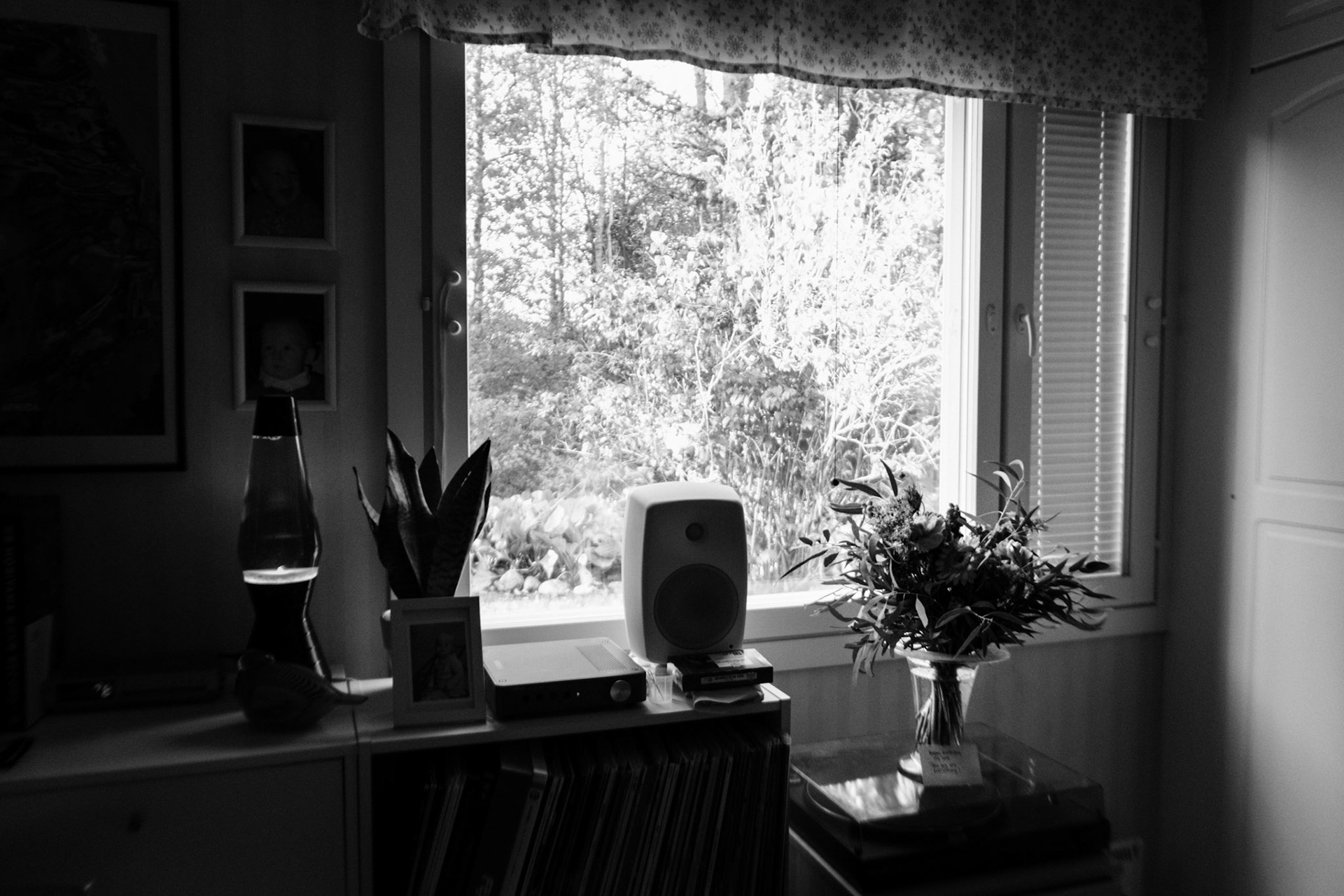 A black-and-white photo of a flower bouquet on a record player, next to a window that illuminates natural light inside the room.
