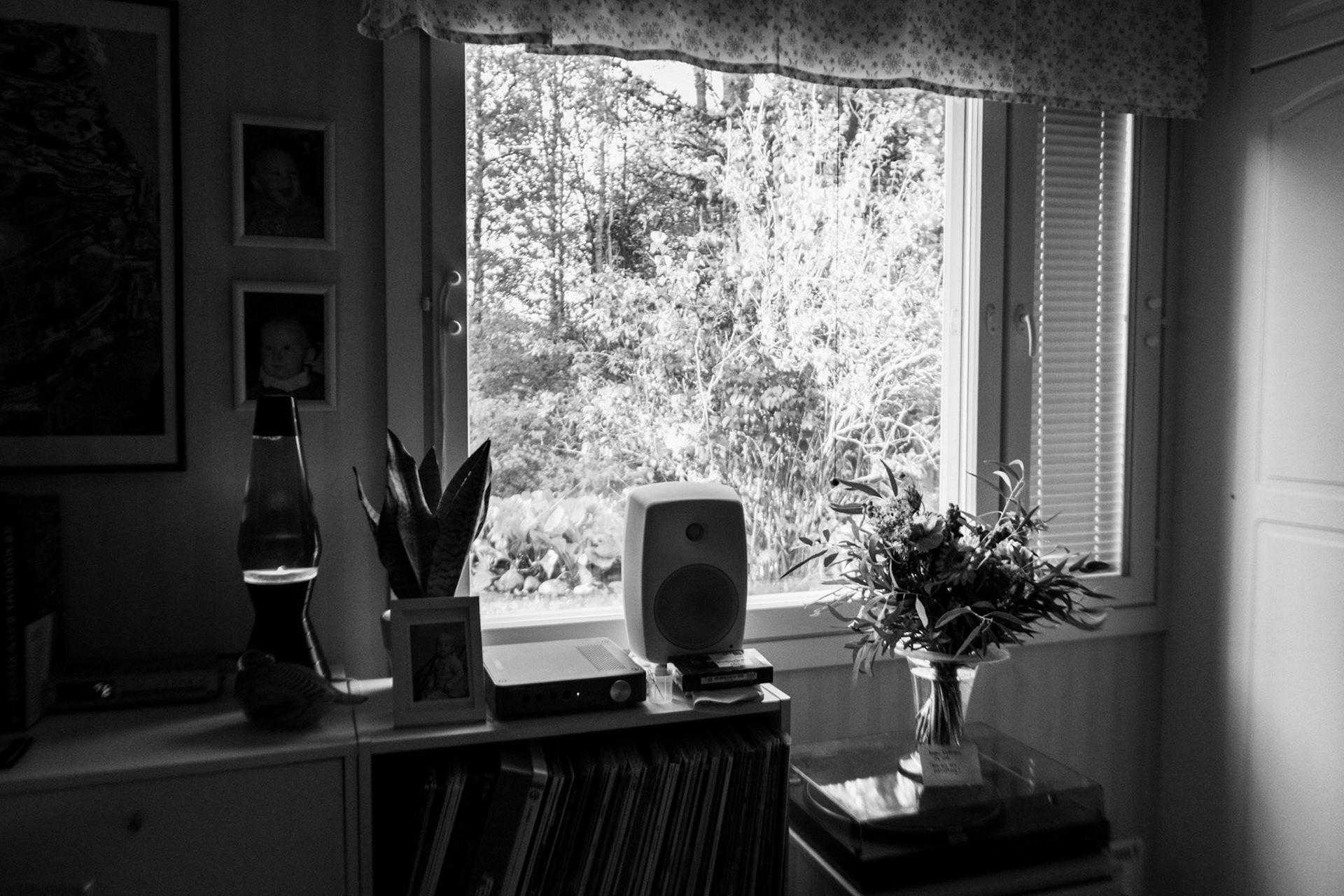 A black-and-white photo of a flower bouquet on a record player, next to a window that illuminates natural light inside the room.