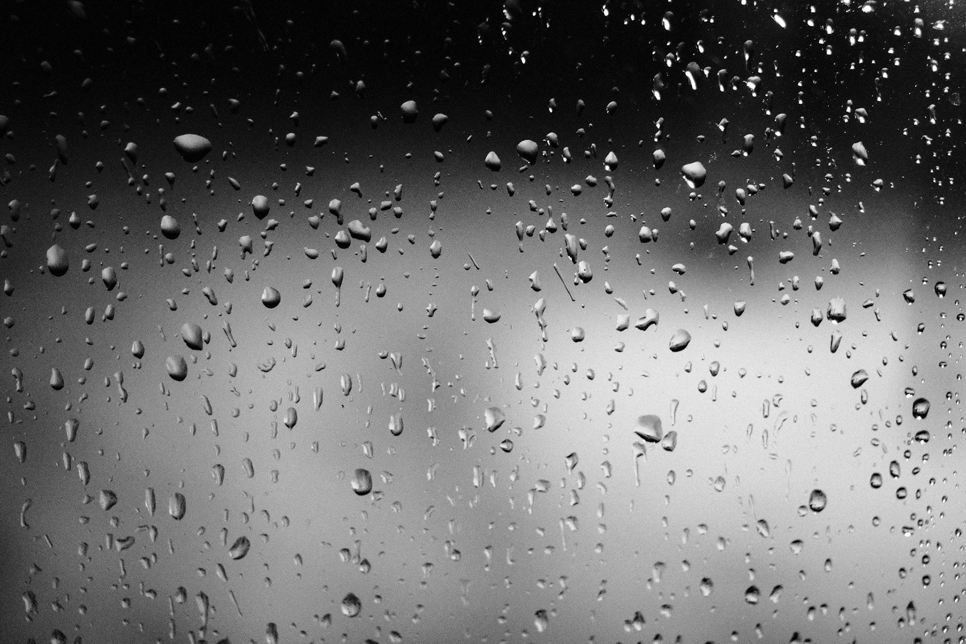 A black and white close-up photo of raindrops on a windowpane.