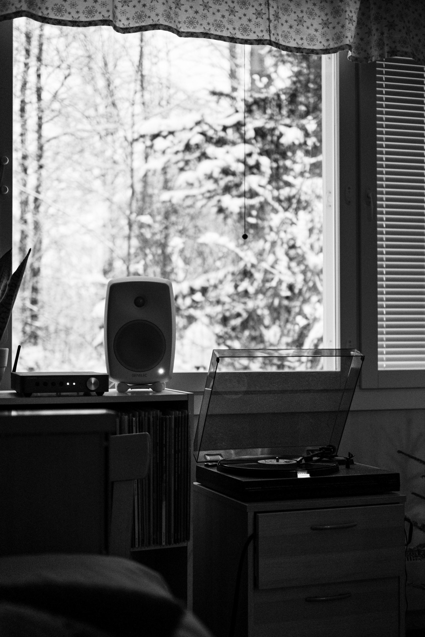 A black-and-white photo of a turntable playing a vinyl record. A snowy landscape is seen from the window in the background.