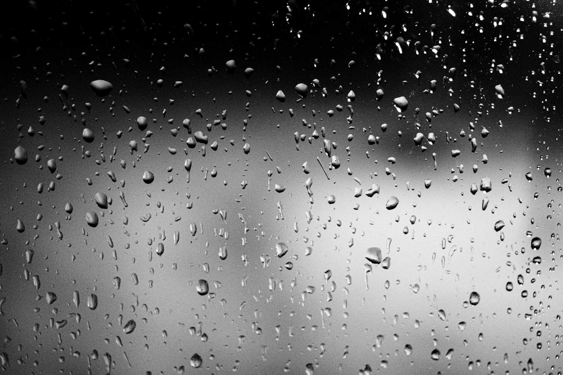 A black-and-white close-up photo of raindrops on a windowpane.