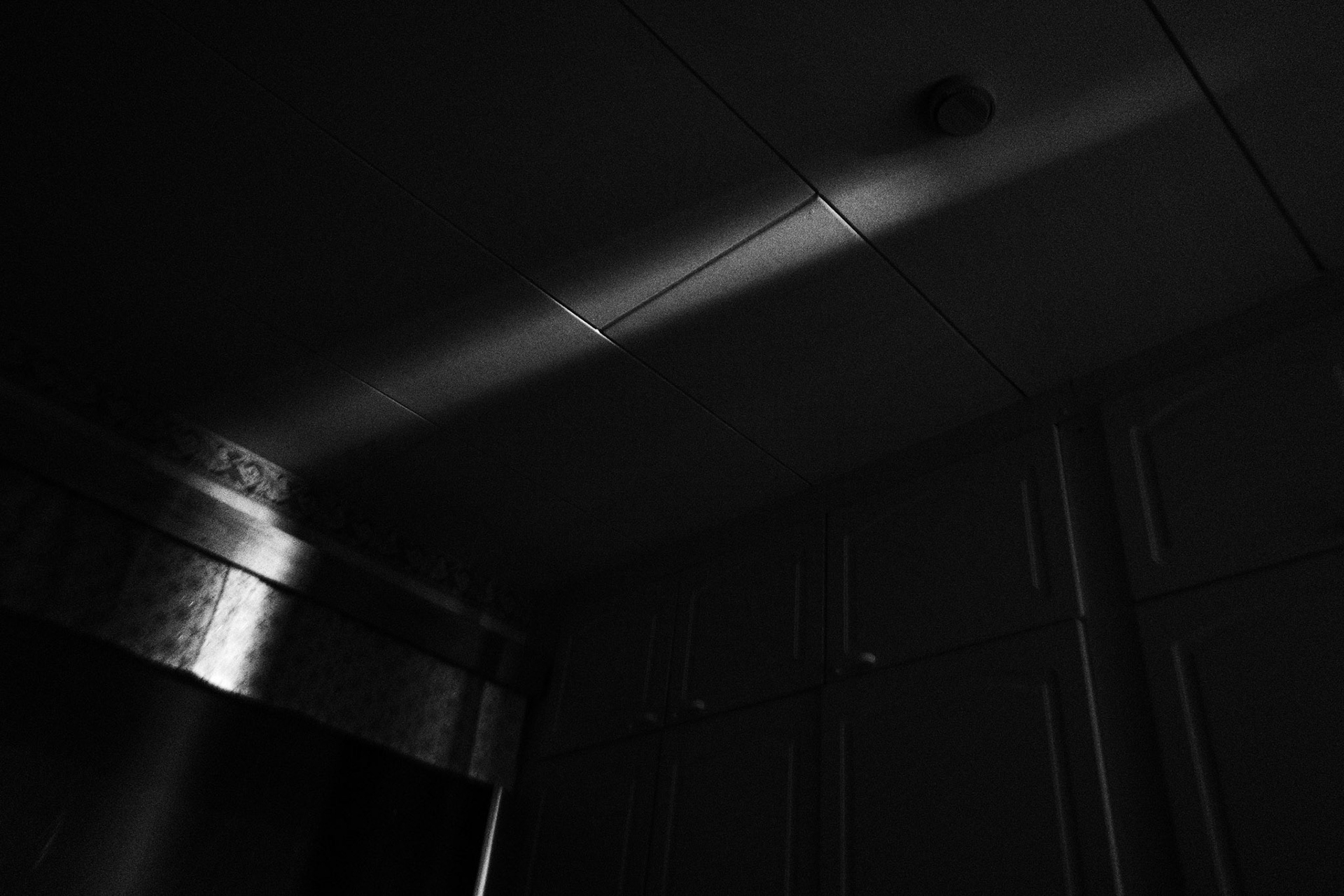 A black and white high contrast photograph showing a ray of light against the ceiling of a dark bedroom.