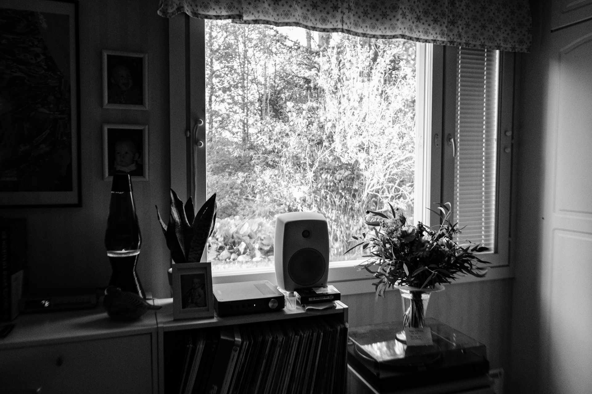A black and white photo of a flower bouquet on a record player, next to a window that illuminates natural light inside the room.