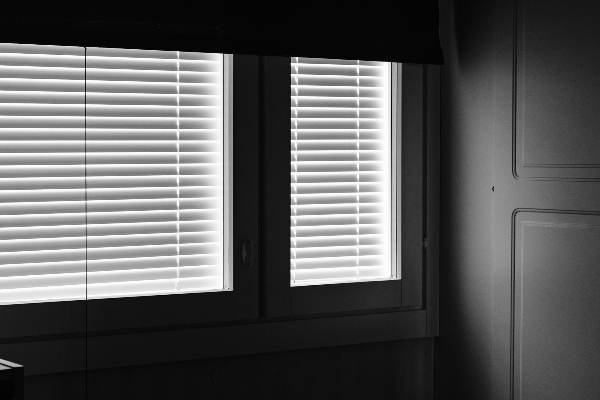 A black and white photo of closed blinds and a partially lowered blackout curtain.