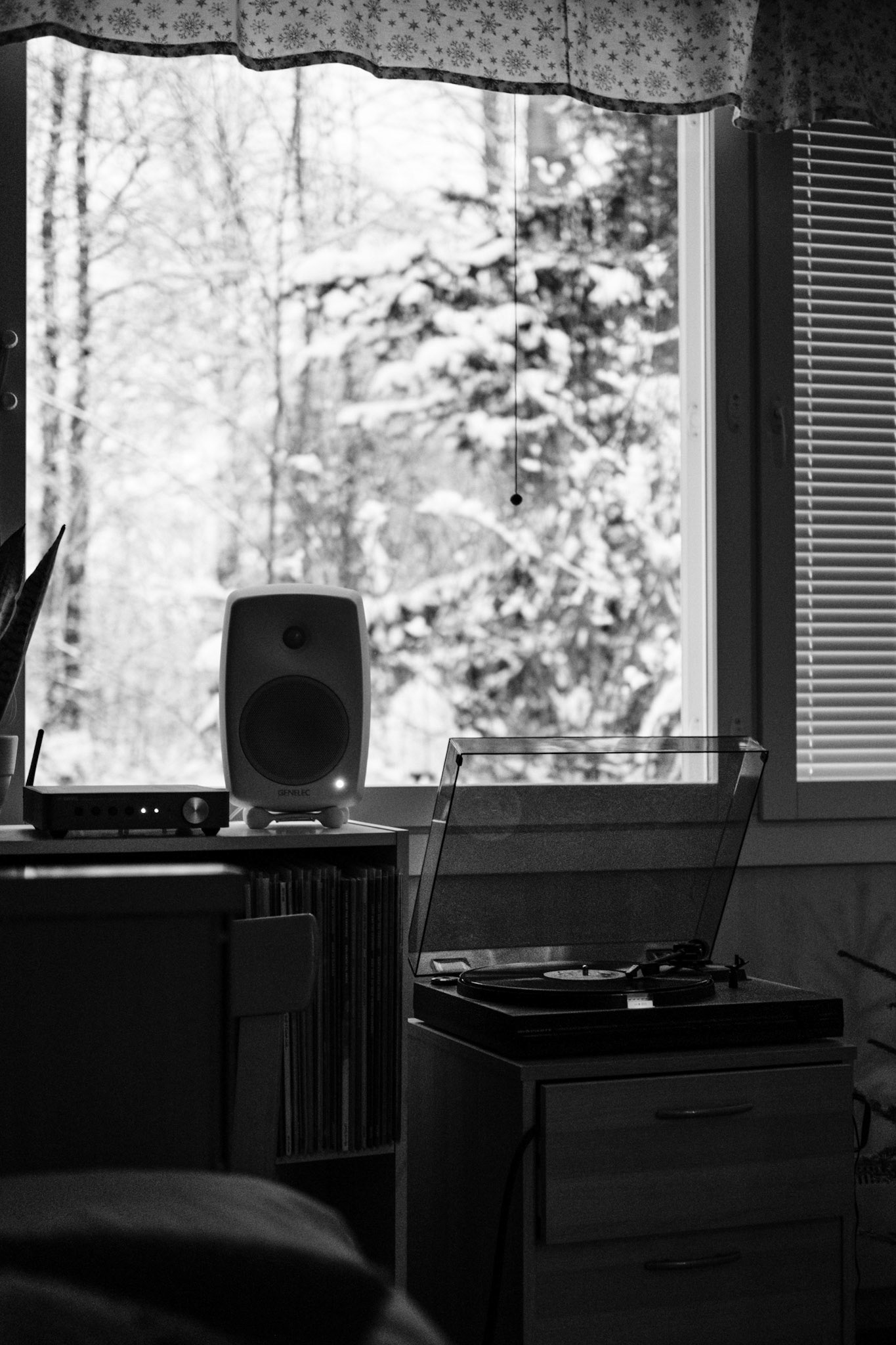 A black-and-white photo of a turntable playing a vinyl record. A snowy landscape is seen from the window in the background.