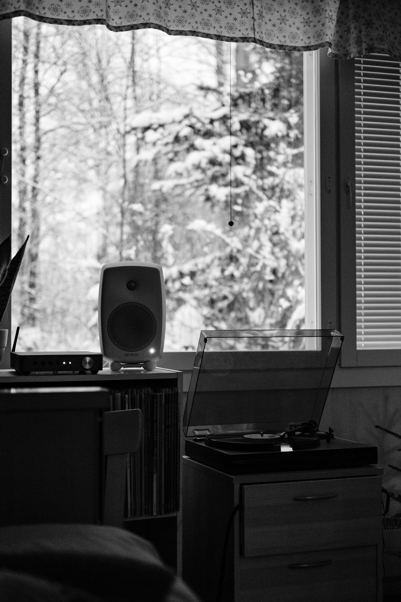 A black and white photo of a turntable playing a vinyl record. A snowy landscape is seen from the window in the background.