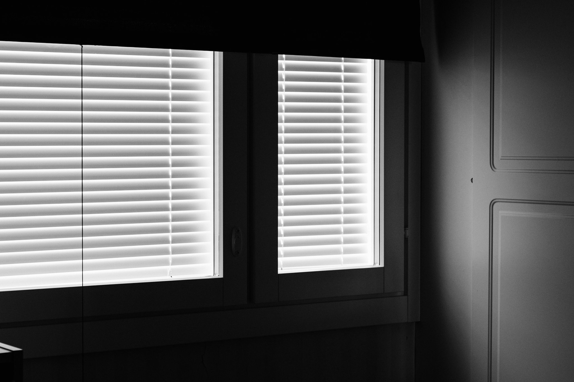 A black-and-white photo of closed blinds and a partially lowered blackout curtain.