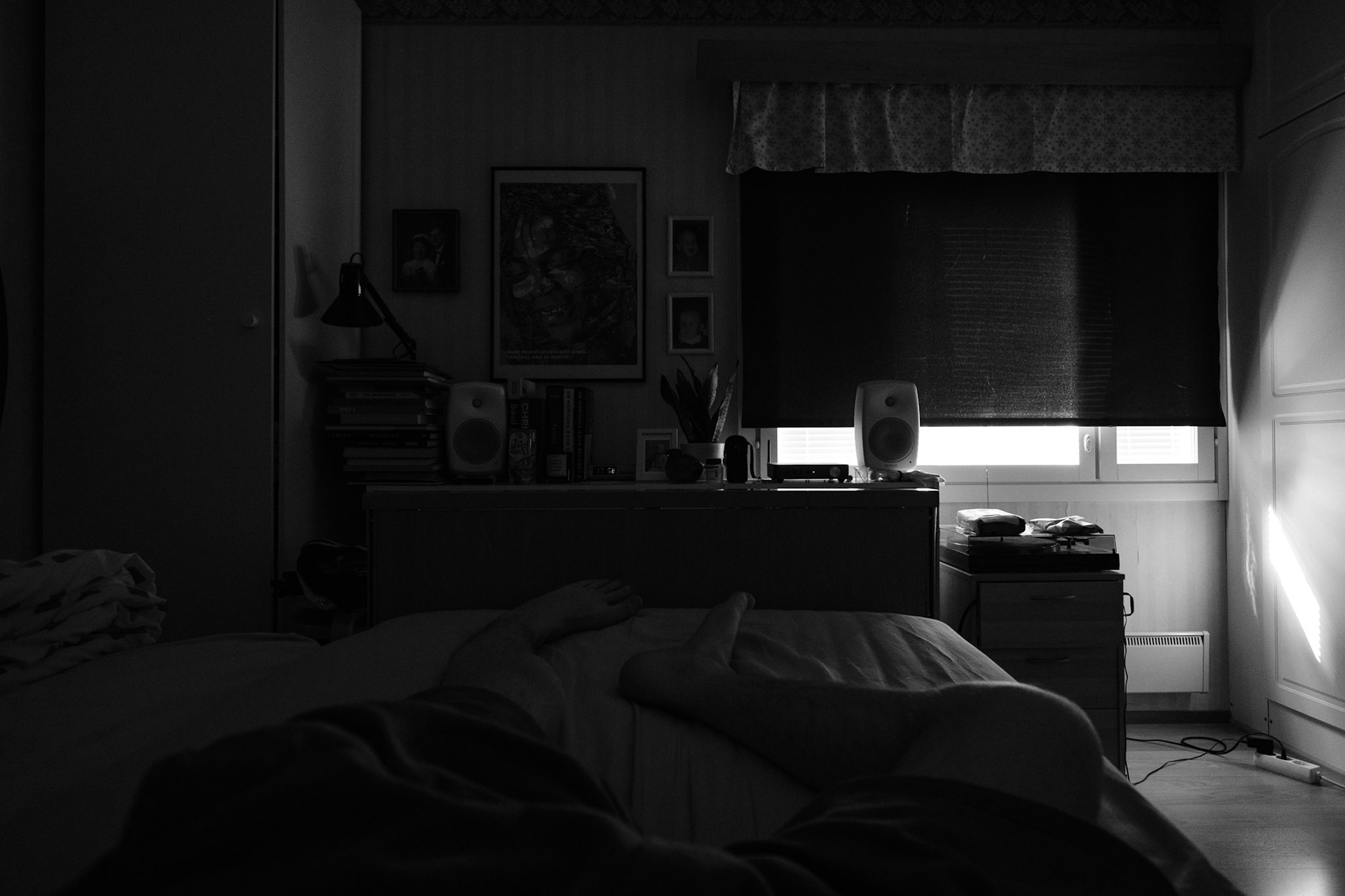 A black and white photo taken from Niko’s point of view while he lies on his bed. The blackout curtain almost fully covers the window.