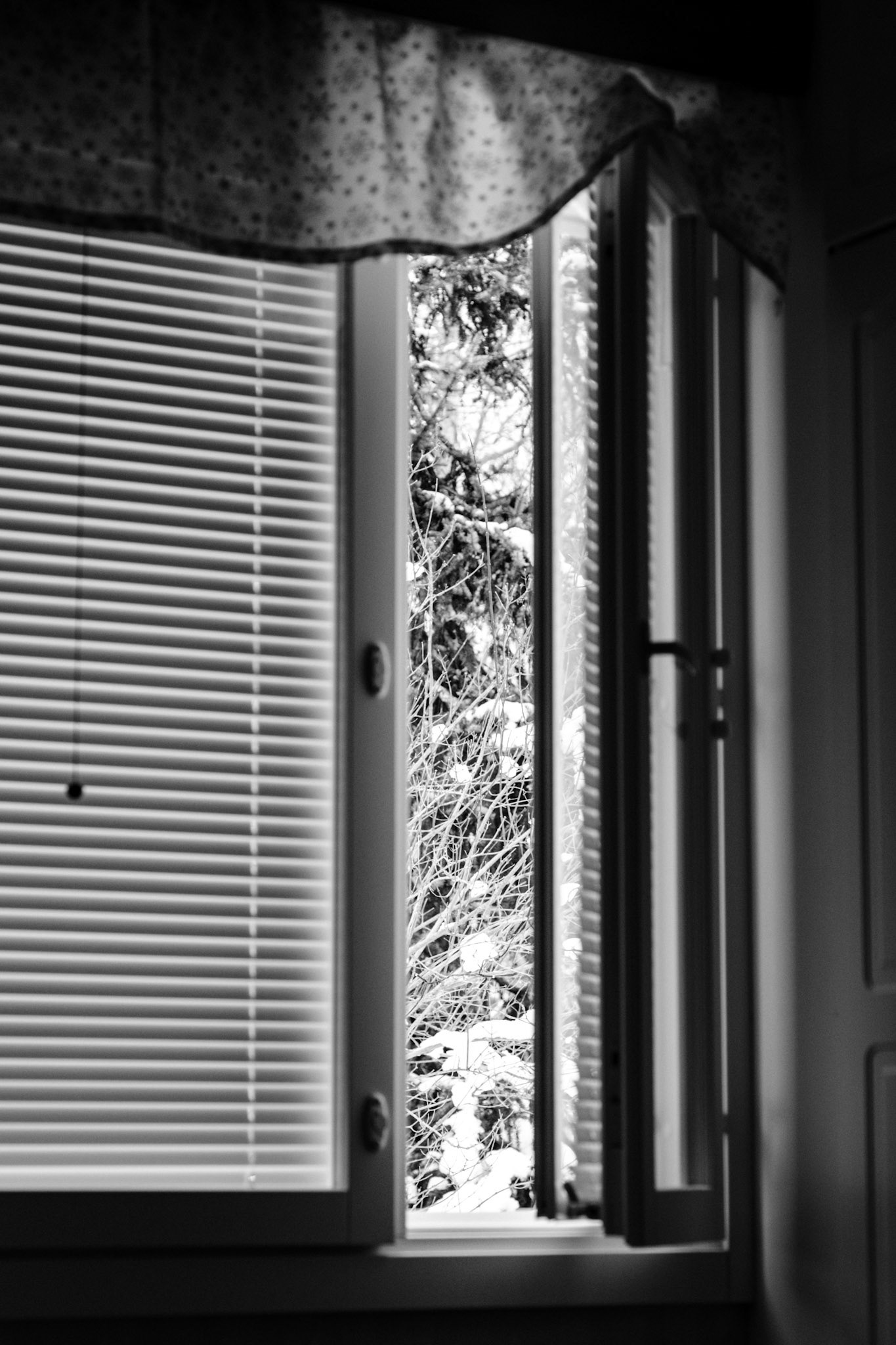 A black-and-white photo of an open side window in an otherwise dark bedroom. 