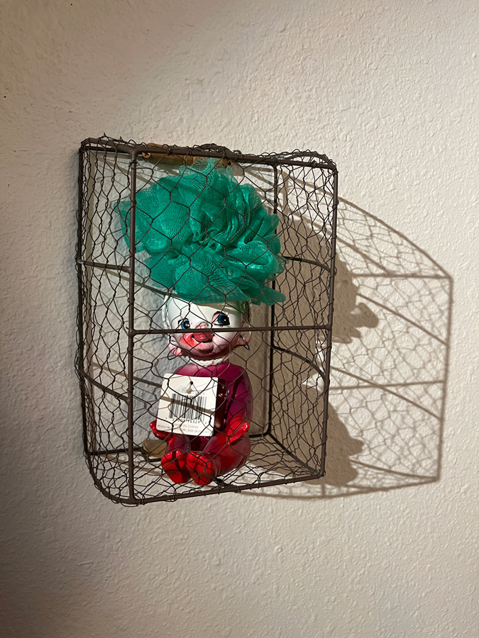 Tricks and Treatment, 2022, Spray paint on Japanese Americana ceramic doll with loofah and price tag inside wire basket, 8 x 8 x 8 inches