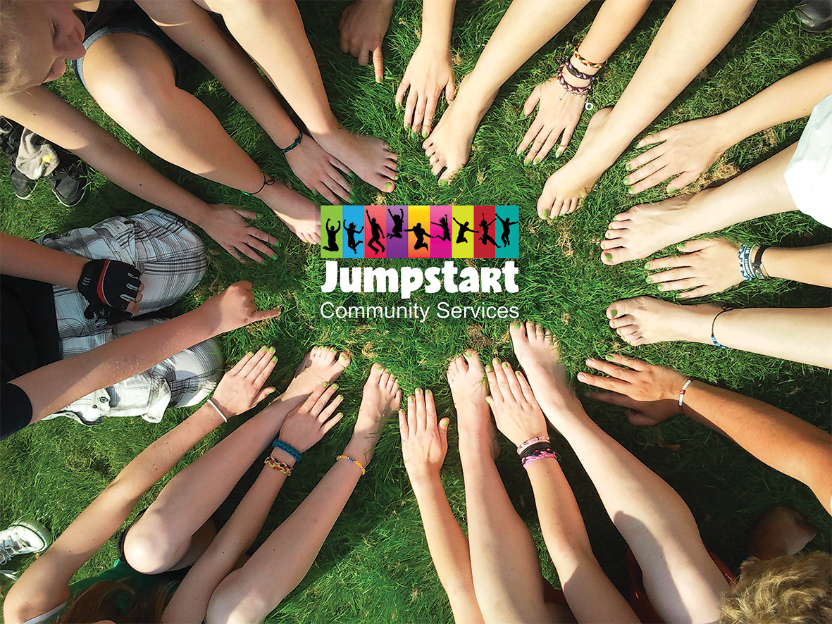 A circle of many hands and feet on grass with the Jumpstart Community Services logo in the centre.