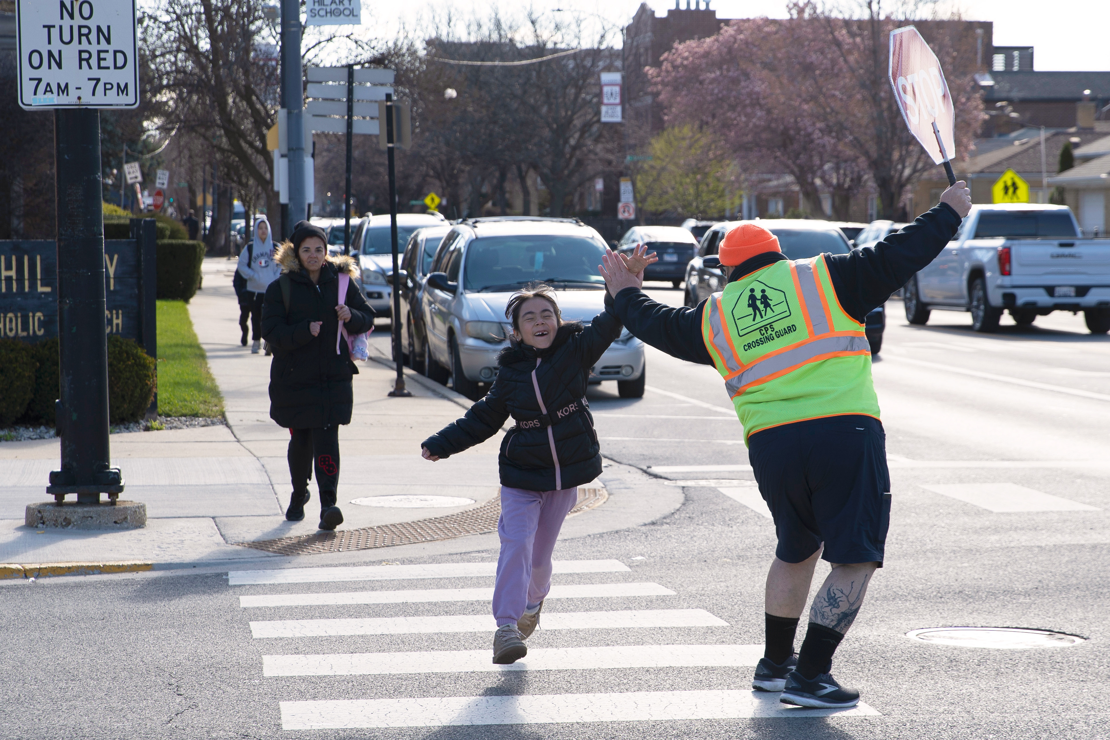 Chicago Public Schools crossing guard Joe Sass high fives a student walking to Jamieson Elementary School in Chicago on April 7, 2026. Building community relations is just one of the many roles crossing guards have.