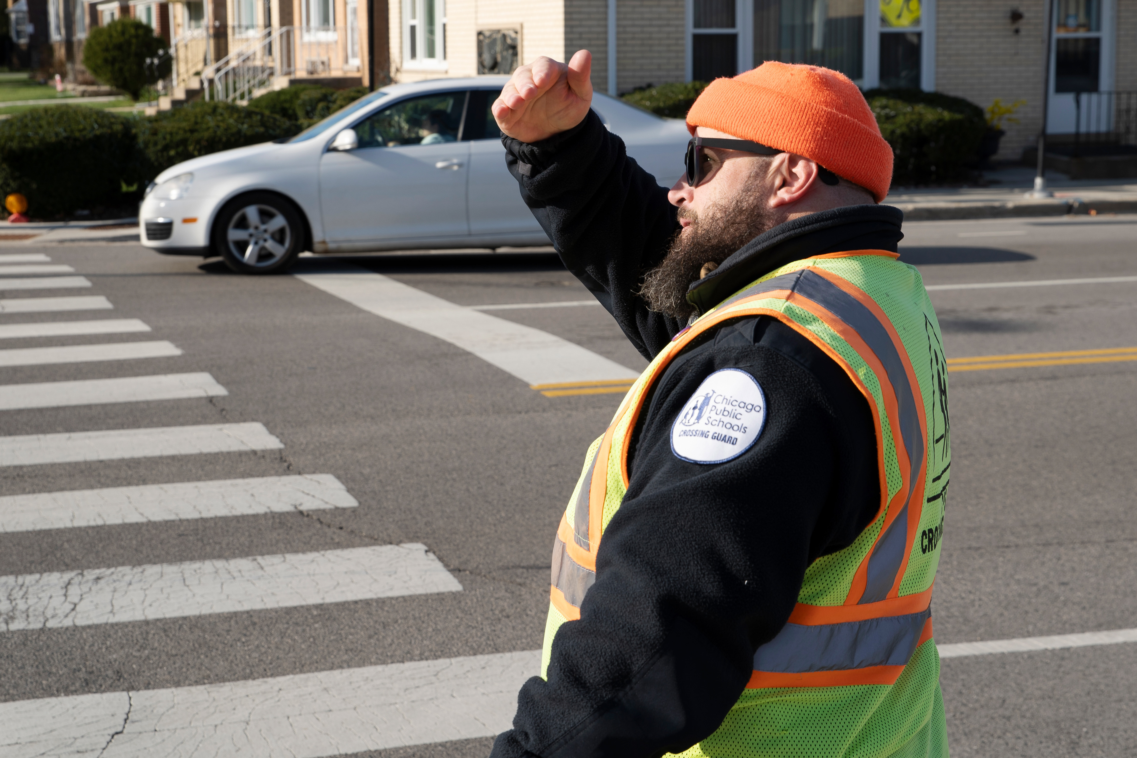 Chicago Public Schools crossing guard Joe Sass shields his eyes against the bright morning sun at the intersection of North California Avenue and West Bryn Mawr Avenue in Chicago on April 7, 2026. According to Sass, glare from the morning sun is the leading cause of accidents involving students walking to school at his intersection.
