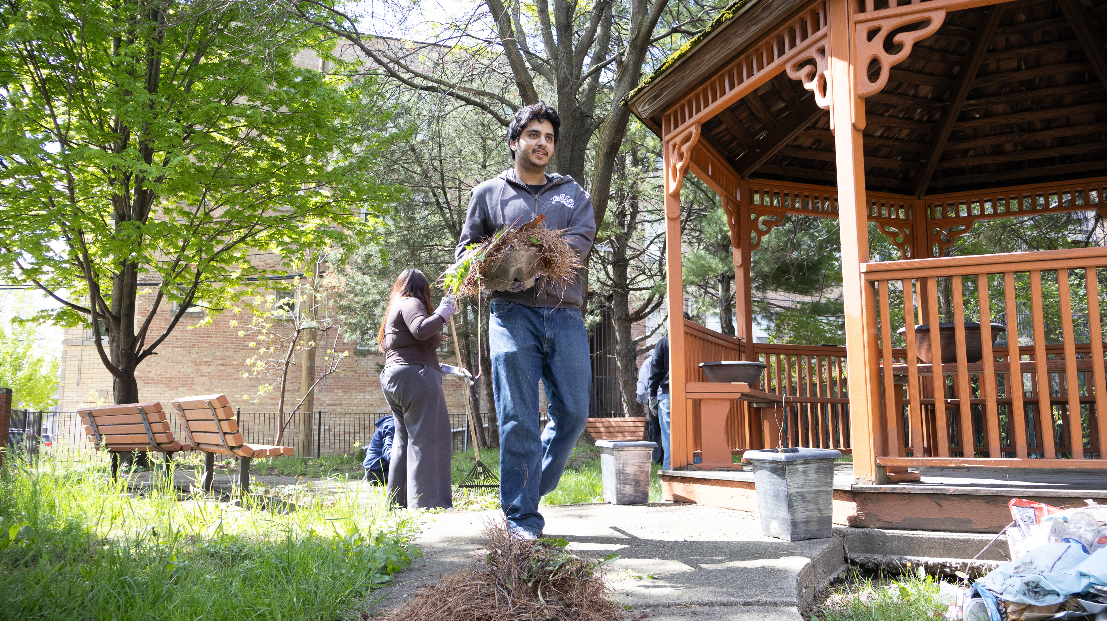Yash Modi, a DePaul sophomore, carries a shovel filled with pine needles and leaves to a designated pile at the Maypole Block Club community garden in West Garfield Park, Chicago on Saturday, May 2, 2026. Modi performed yard work as a Vincentian Service Day volunteer.
