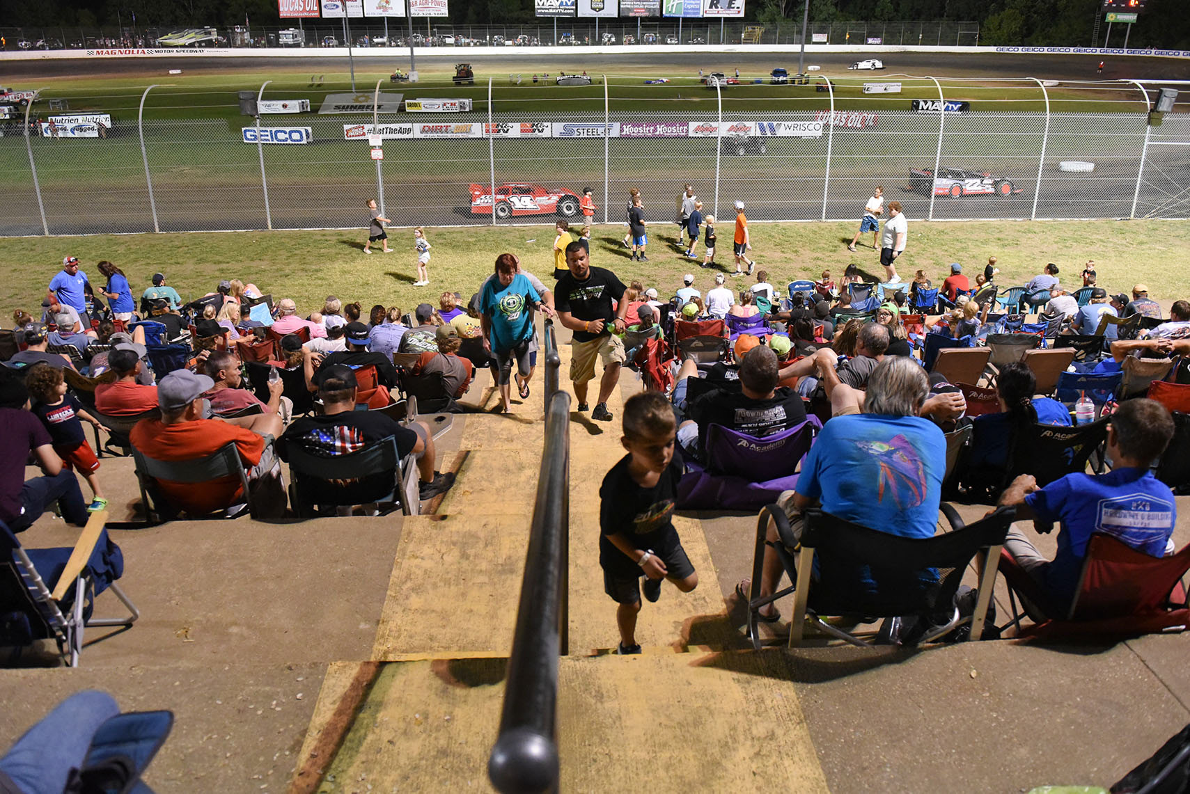 People sit in the crowd and kids play on the grass during the General Tire Clash at the Mag on June 20 at Magnolia Motor Speedway in Columbus. When the next race began, all the kids returned to their seats to watch with their families.