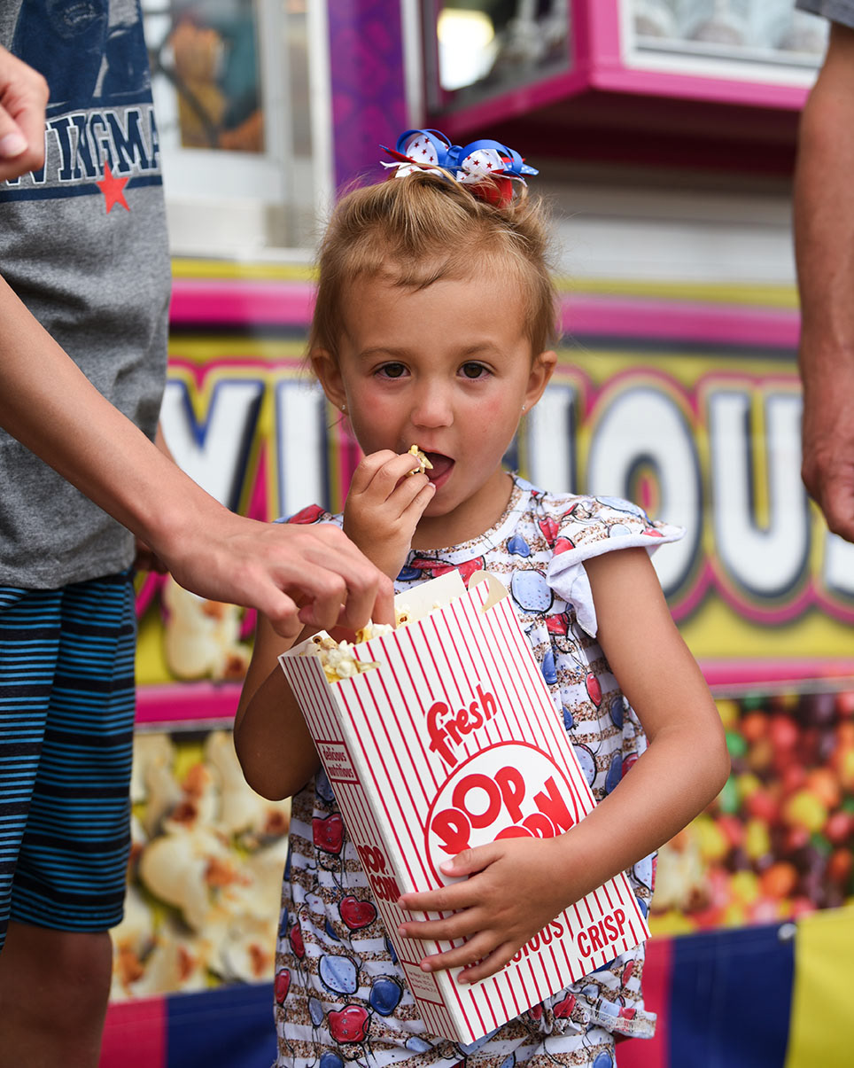 Lucy Kate Plant, 4, eats popcorn snacks on July 4 at the Crescent City Carnival set up off of Highway 45 in Columbus. Before visiting the carnival Lucy Kate and her family went to a cookout. Next, they headed home to relax.