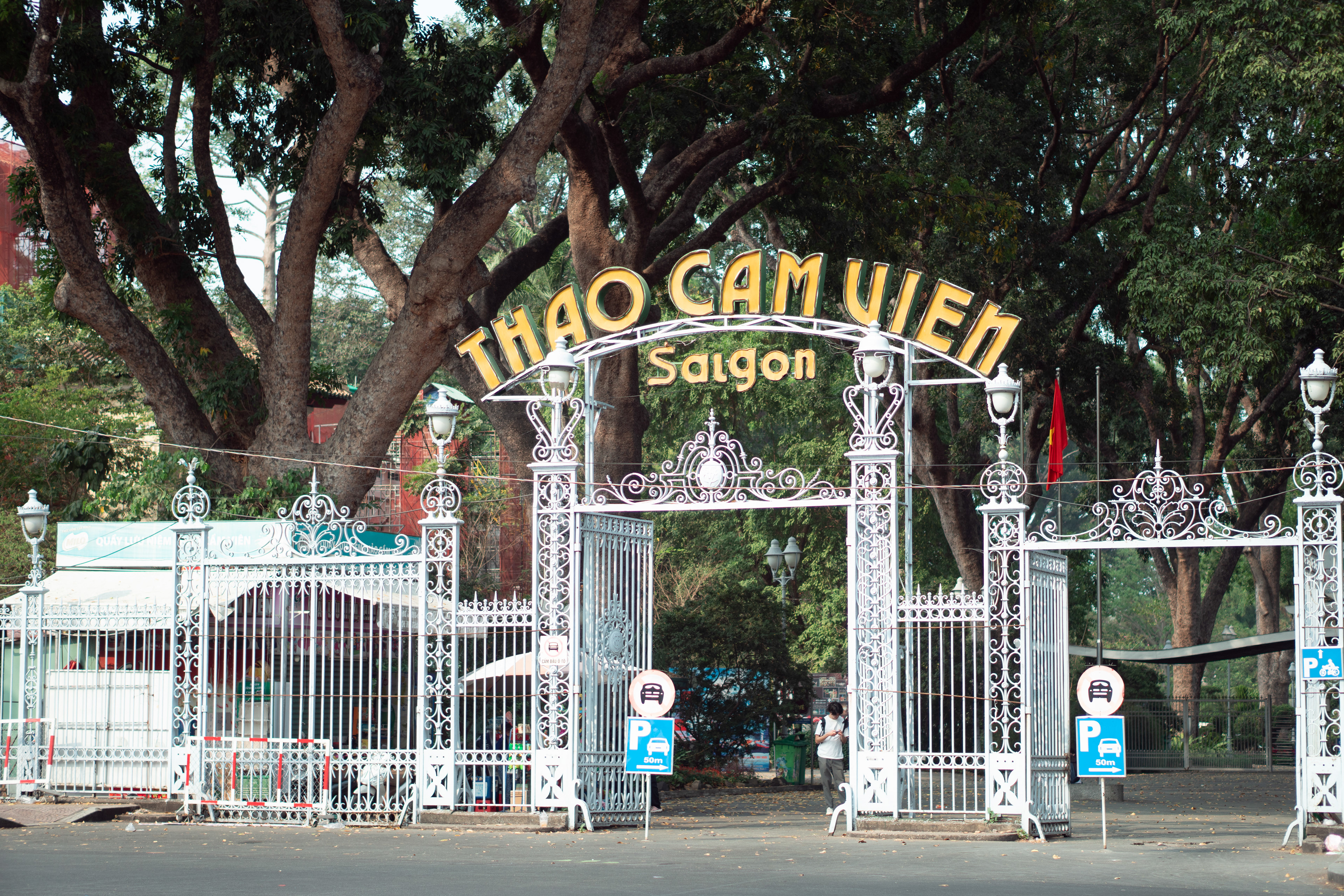 The zoo's entrance gate takes centre stage in the photograph, adorned with vibrant banners and welcoming signage. This initial visual impression sets the tone for an anticipated exploration, as a pathway bordered by lush greenery beckons visitors onward, promising an exciting adventure within.
