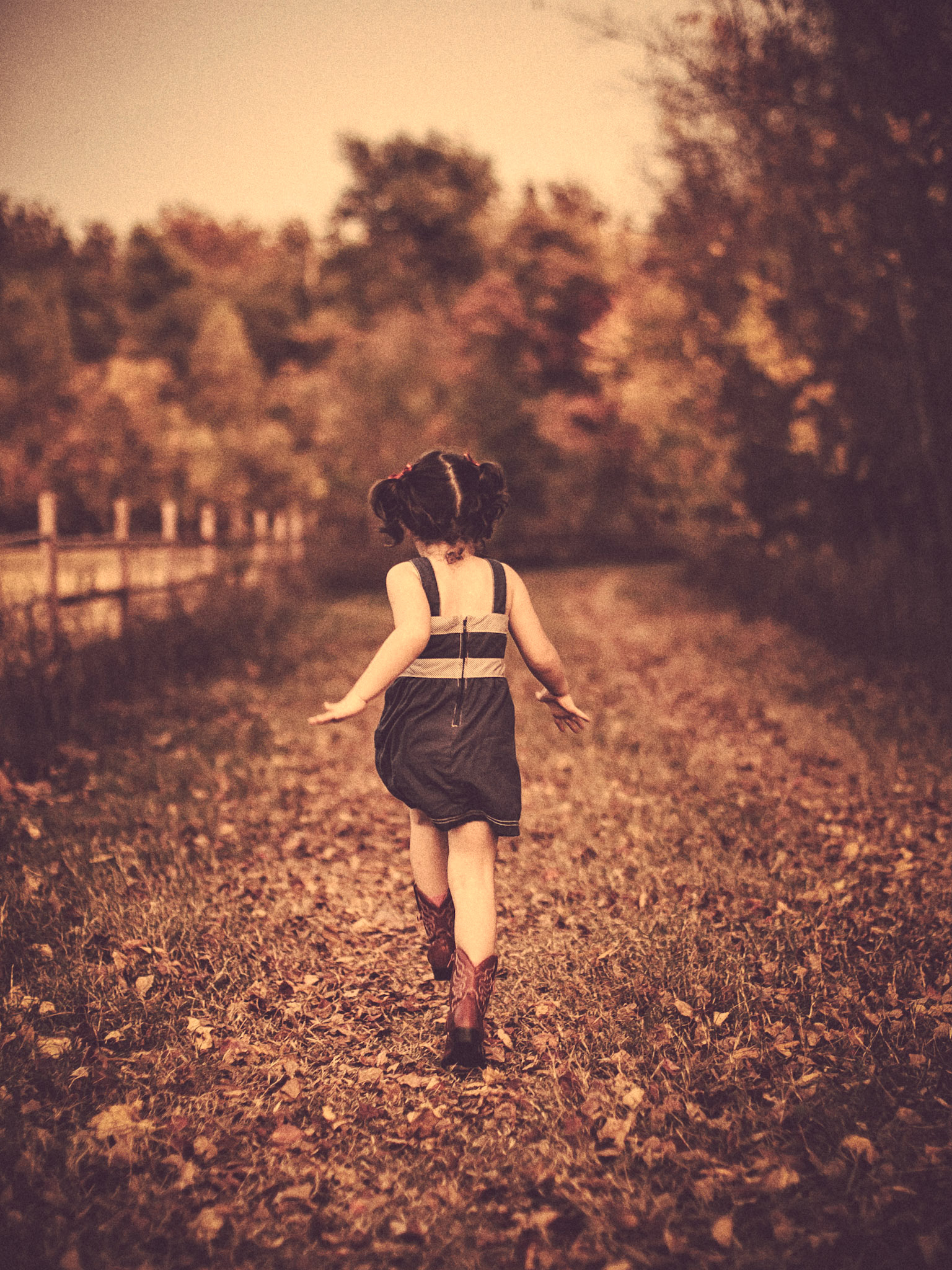 A child running down a country road with fallen leaves.