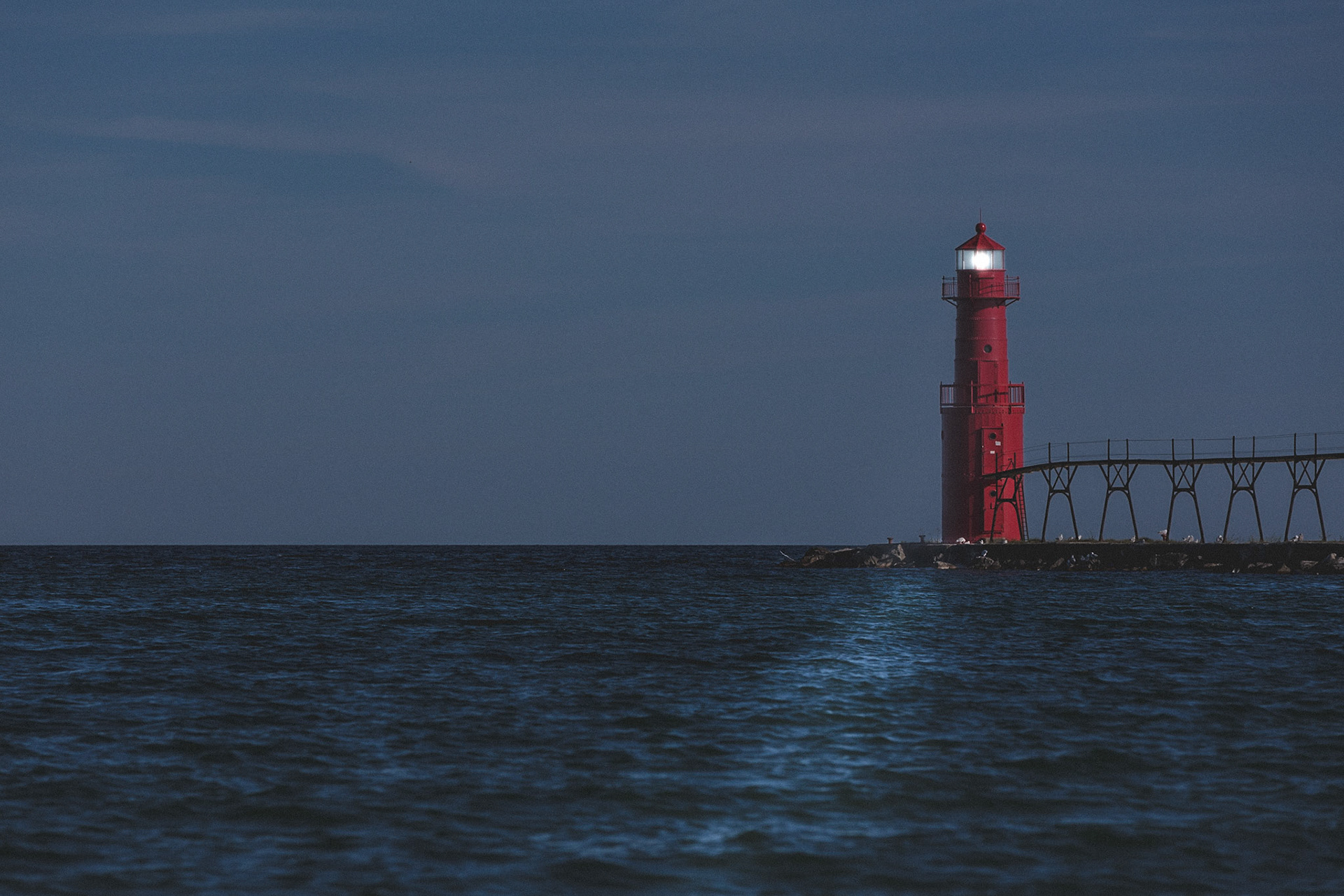 Photograph of a lighthouse on lake michigan at dusk with the light on.